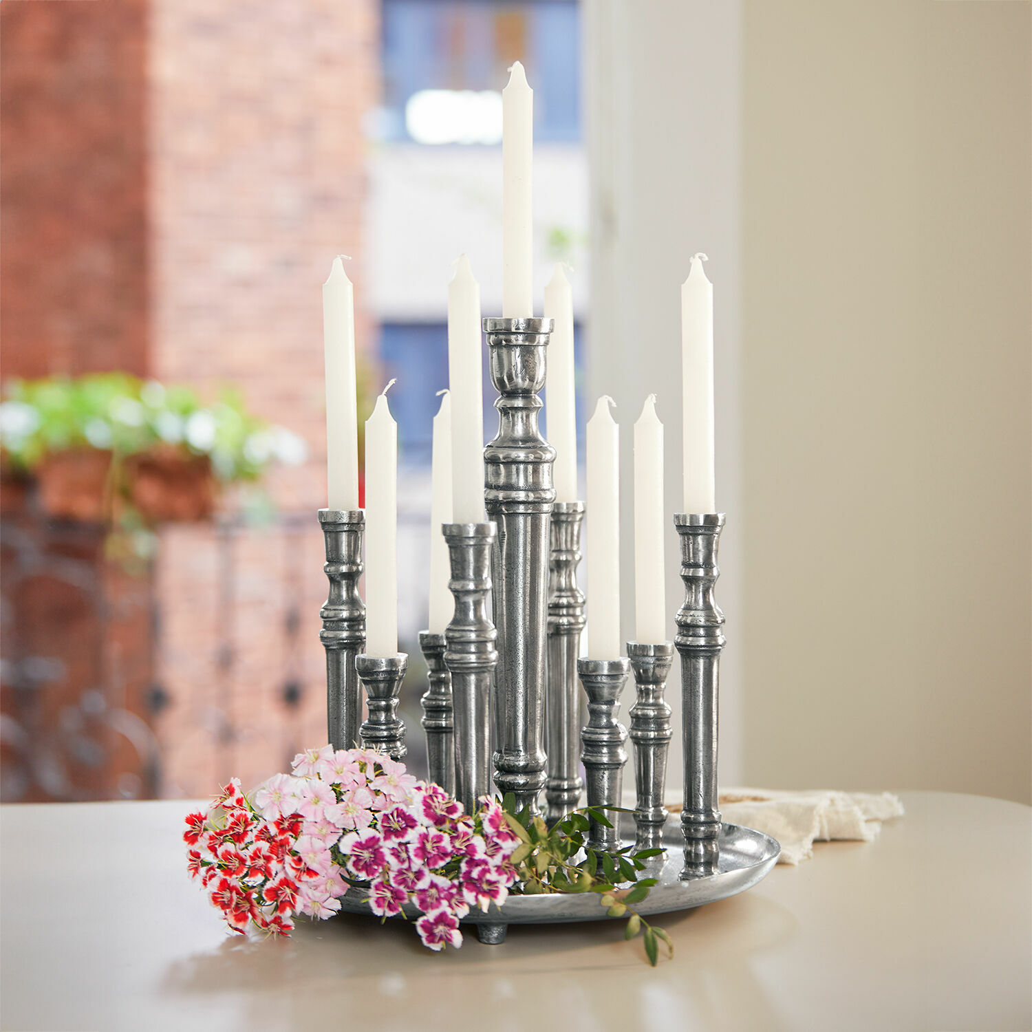 Candelabro Calcot Candelabro de metal con velas blancas y flores coloridas sobre mesa en interior luminoso