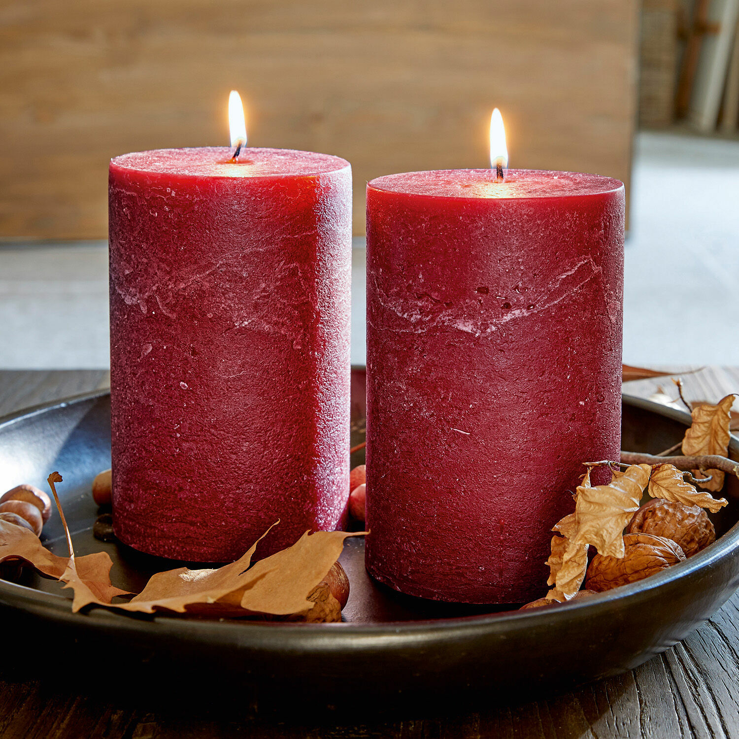 Dos velas rojas de cera en bandeja negra con hojas secas y nueces, decoración otoñal