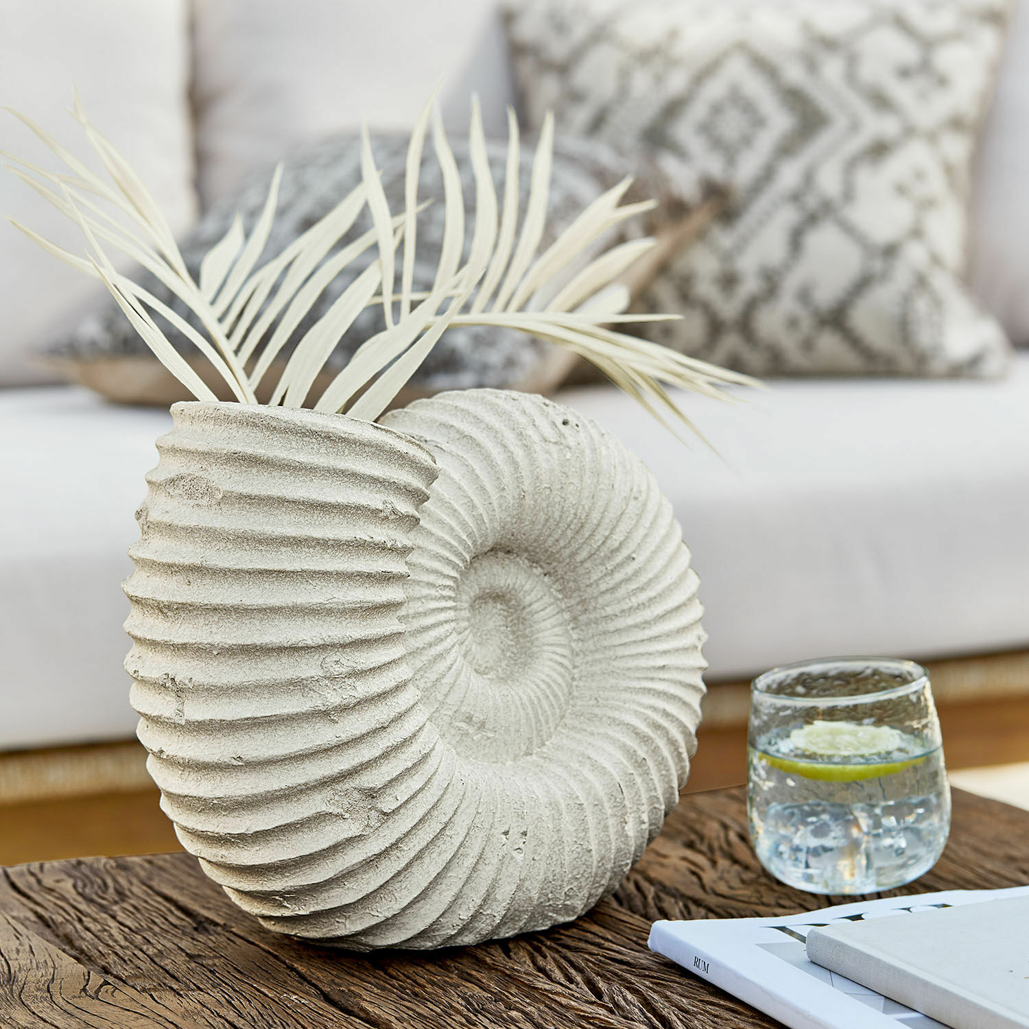 Jarrón Korrellin Jarrón decorativo de hormigón en forma de concha con hojas claras sobre mesa de madera en sala