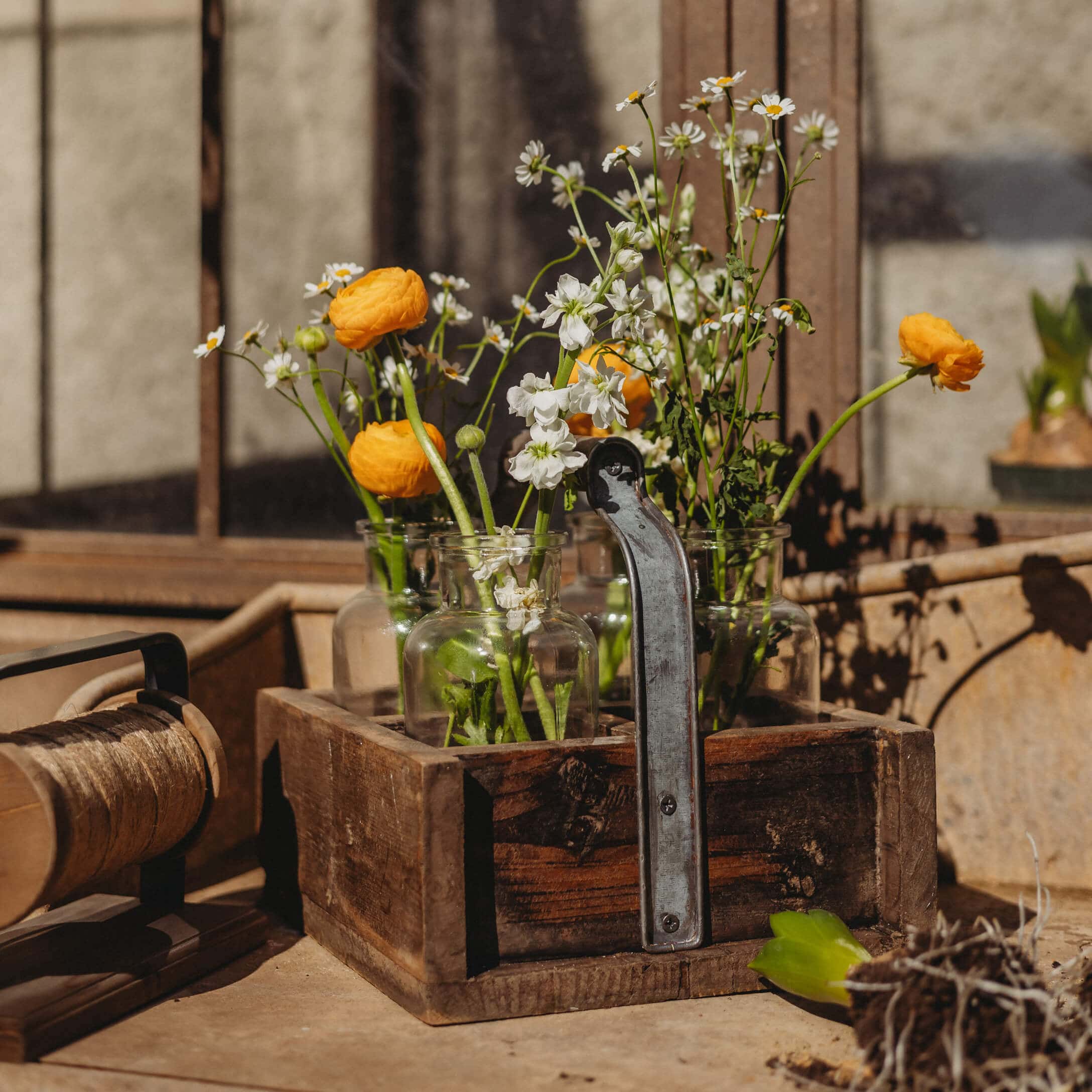 Caja de madera con asa y jarrones de vidrio con flores amarillas y blancas sobre mesa de jardín