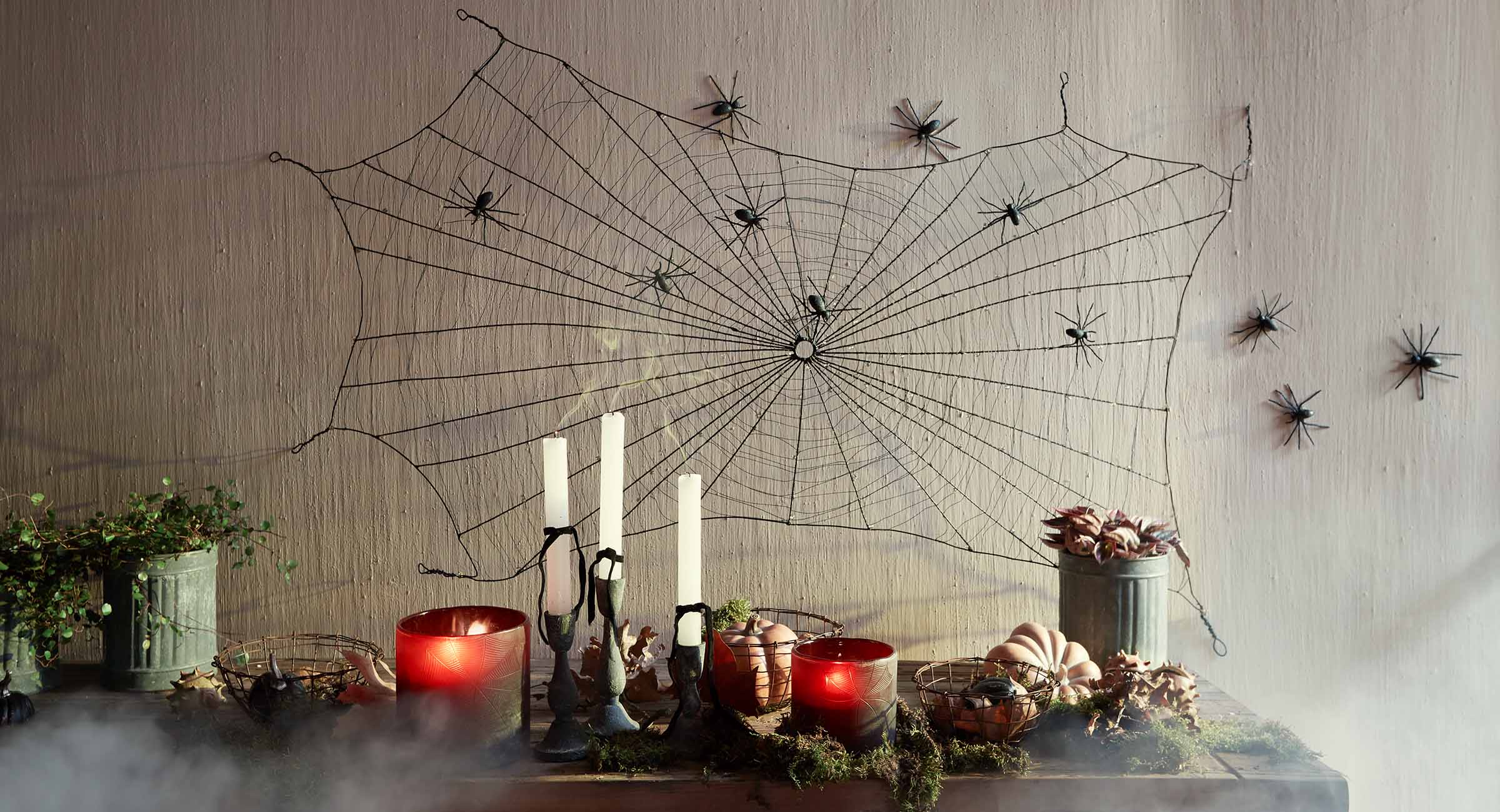 Decoración de Halloween con telaraña negra y arañas en la pared, velas y calabazas sobre la mesa
