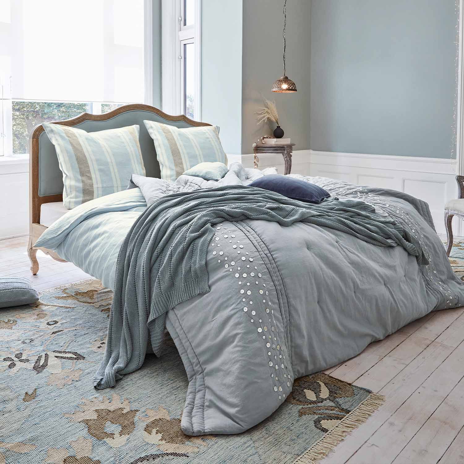 Cama con cabecero de madera y ropa de cama azul claro con manta de punto suave y cojines
