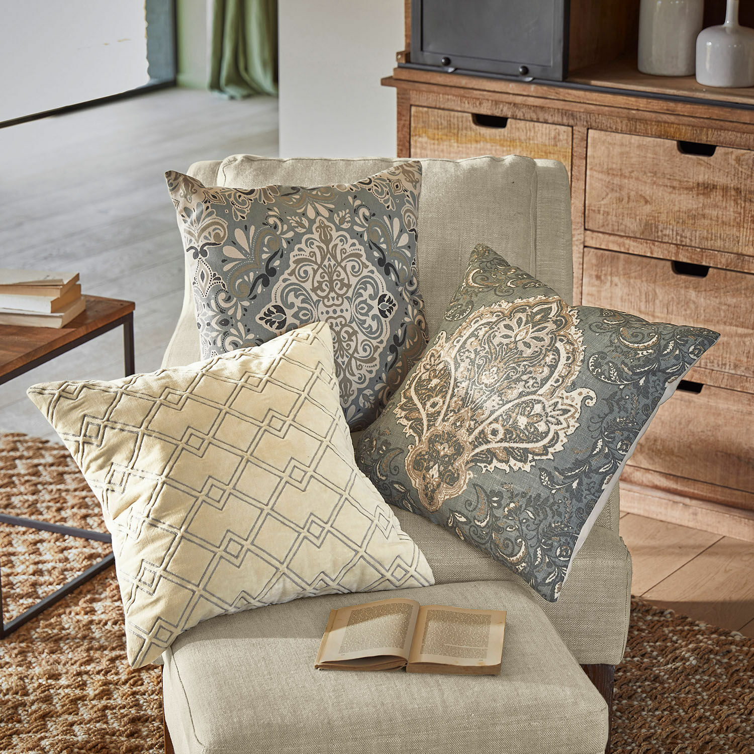 Set de 3 fundas de cojín Madalena Tres cojines decorativos con patrones beige y gris sobre un sillón claro en sala de estar