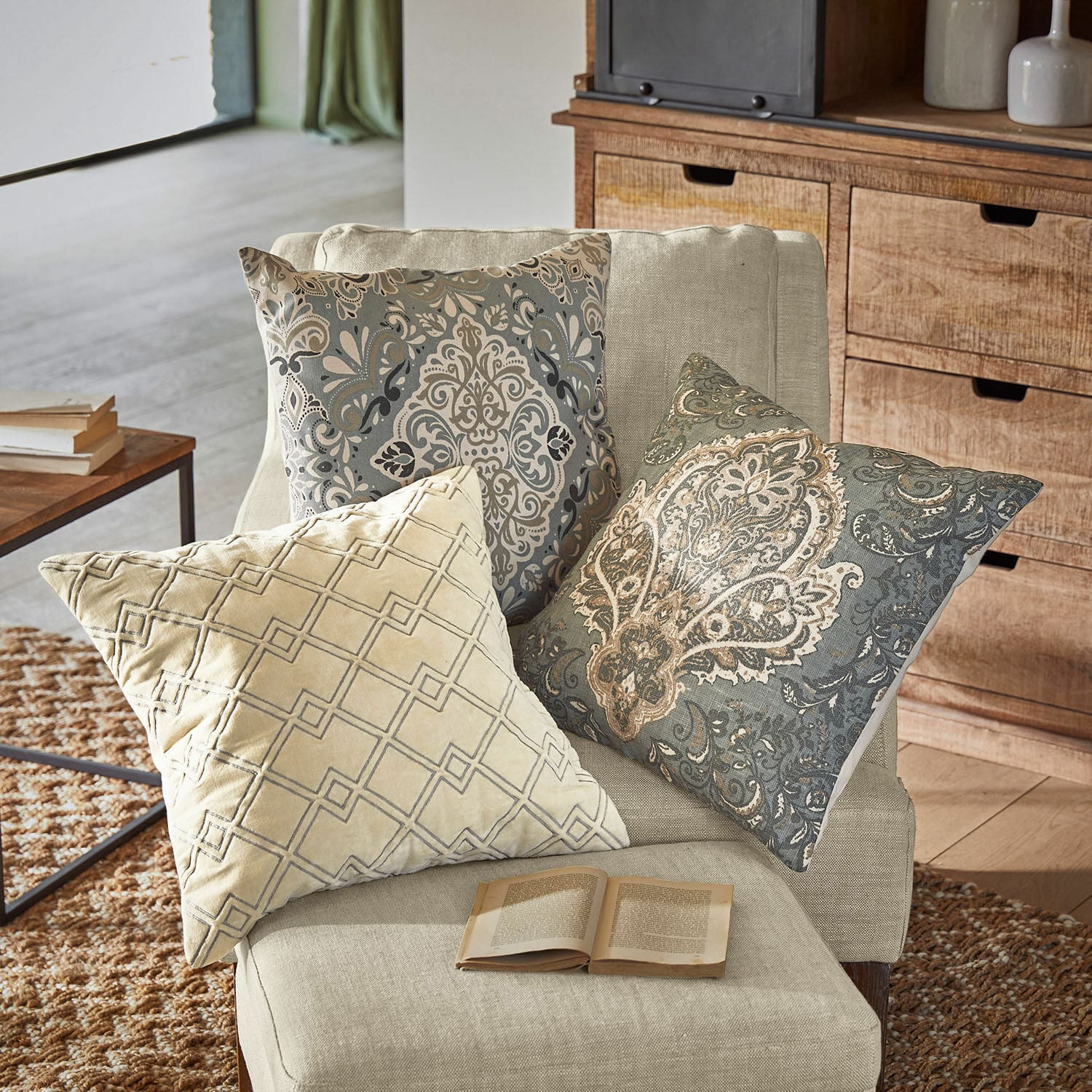 Set de 3 fundas de cojín Madalena Tres cojines decorativos con patrones beige y gris sobre un sillón claro en sala de estar