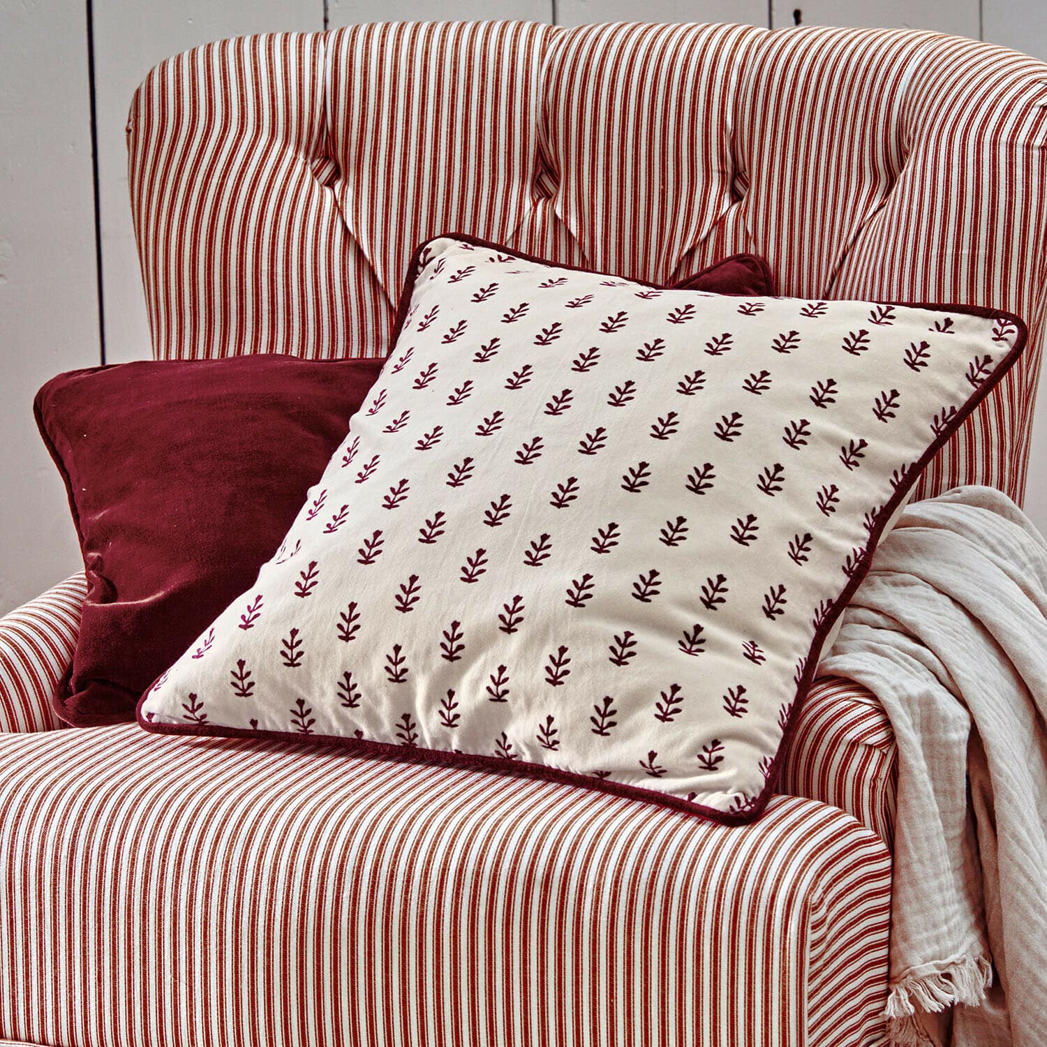 Set de 2 fundas de cojín Eilira Sillón a rayas rojas y blancas con cojines burdeos y manta clara para decoración