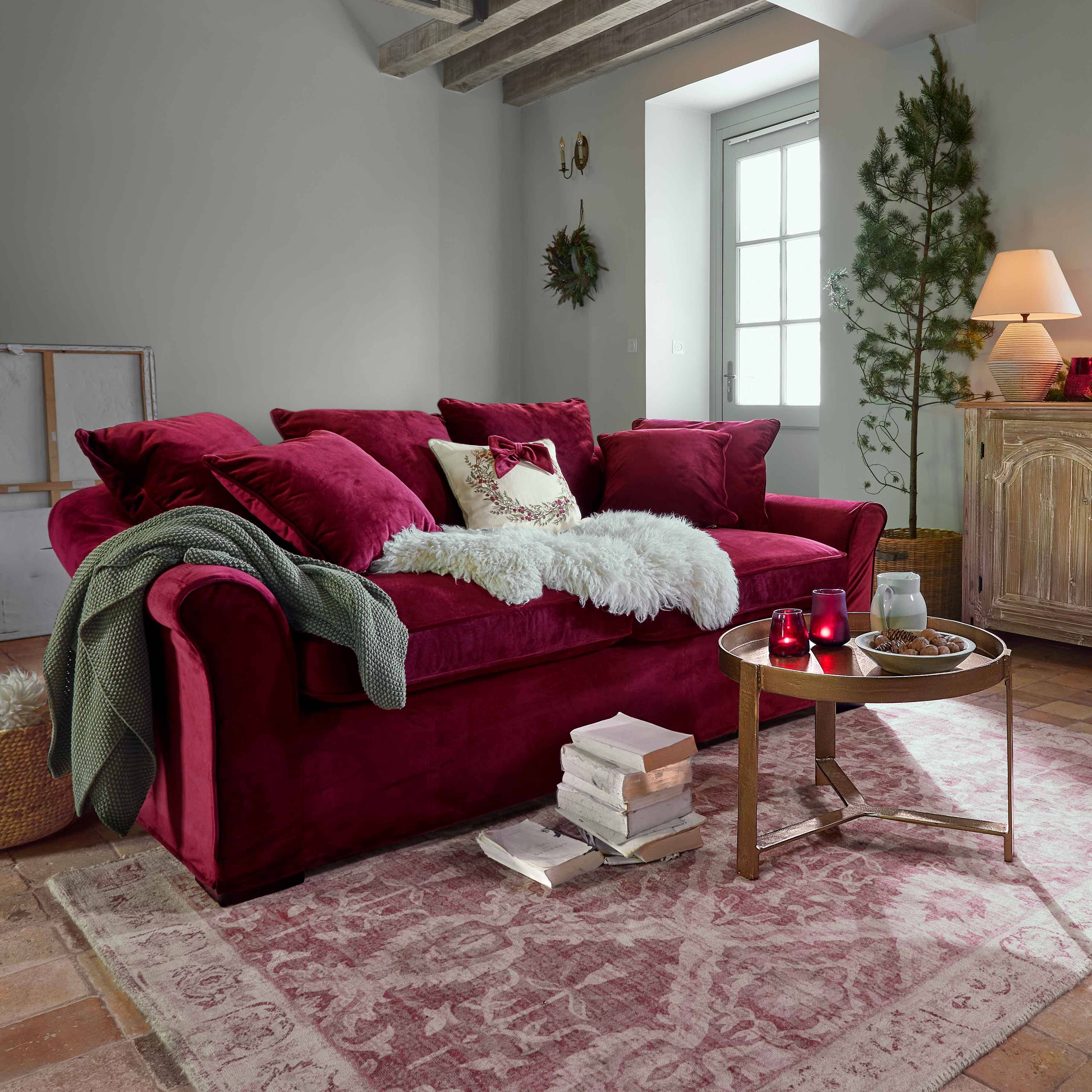 Sofá de terciopelo burdeos con cojines y manta suave en salón acogedor con vigas de madera