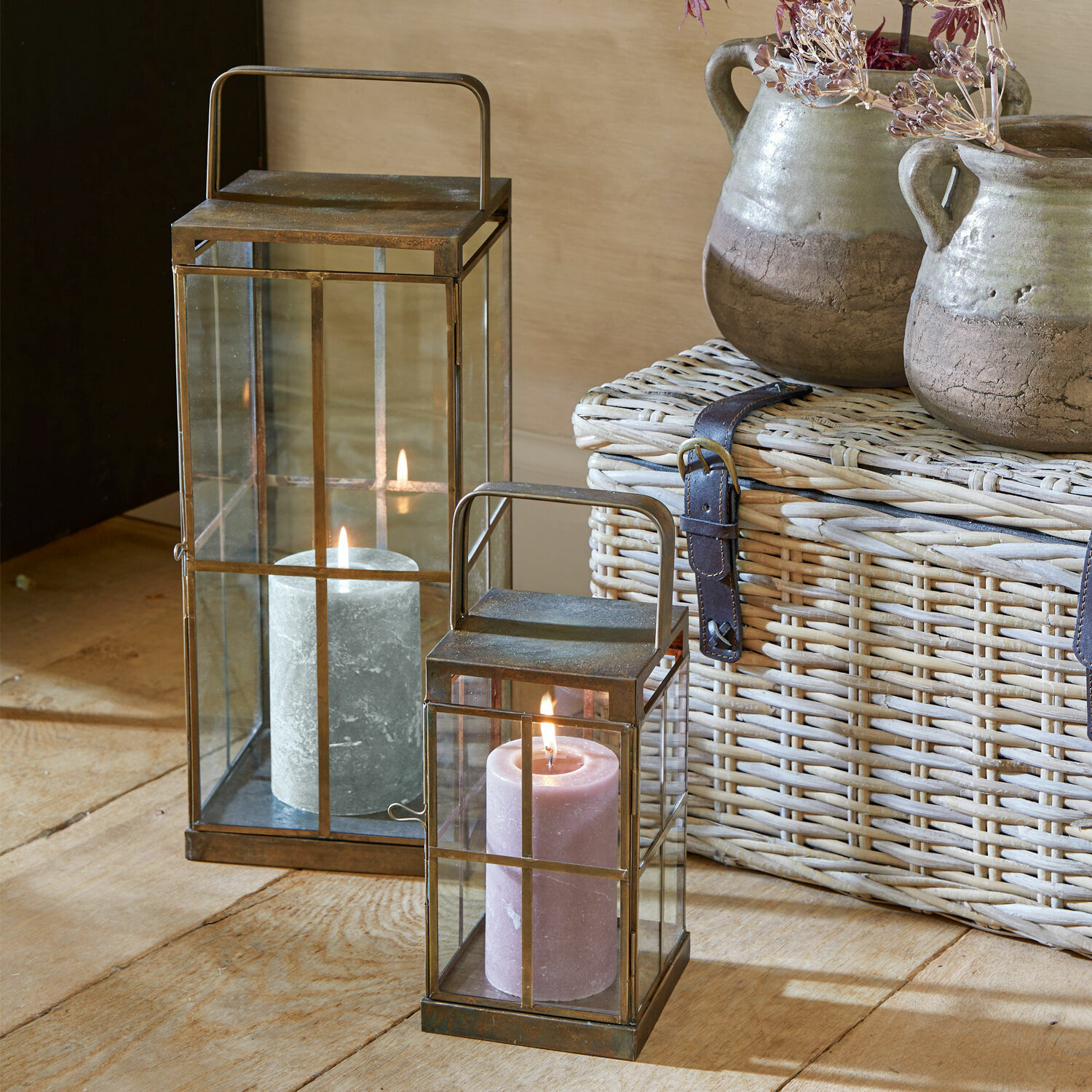 Set de 2 linternas Garrett Park Dos faroles de metal con asas y velas en cajas de vidrio sobre suelo de madera