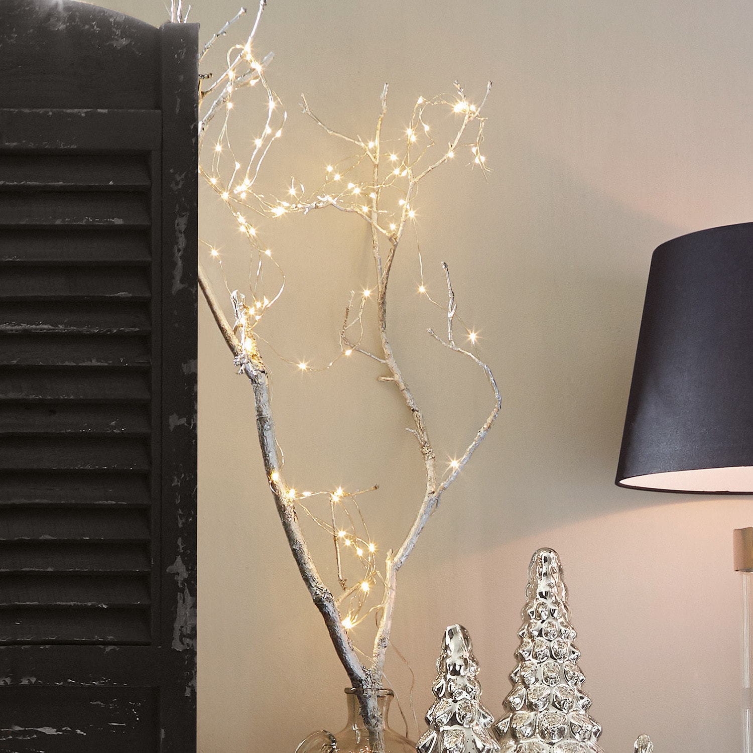 Luces de hadas Loperhet Rama decorativa con luces LED en jarrón transparente junto a adornos navideños plateados y lámpara negra
