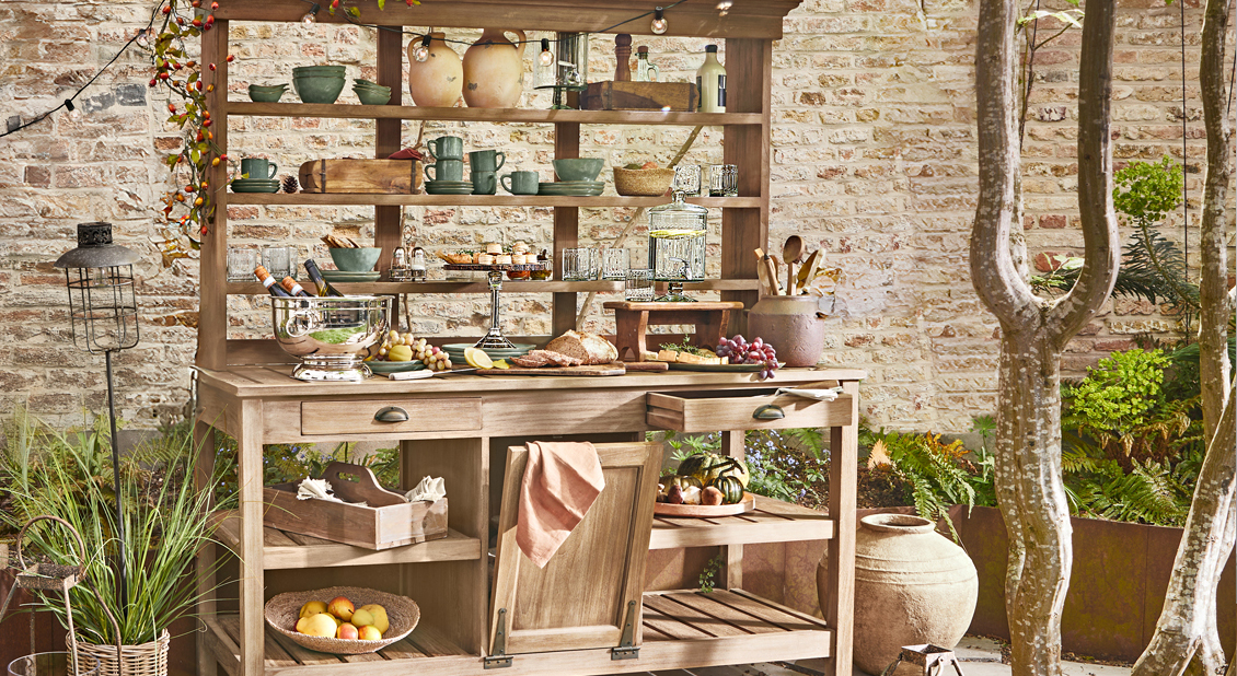 Mueble de jardín de madera con estantes y cajones, decorado con vajilla y comida al aire libre