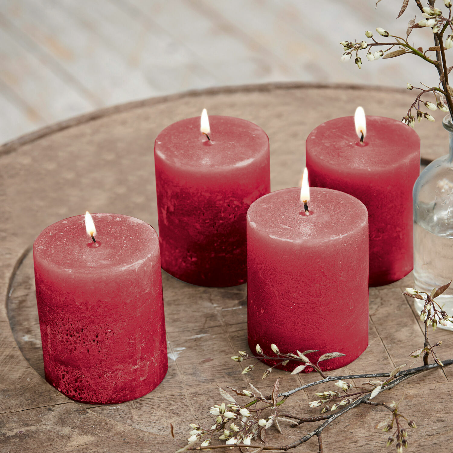 Set de 4 velas Virrans Cuatro velas rojas de cera sobre mesa de madera con decoración floral, ambiente acogedor