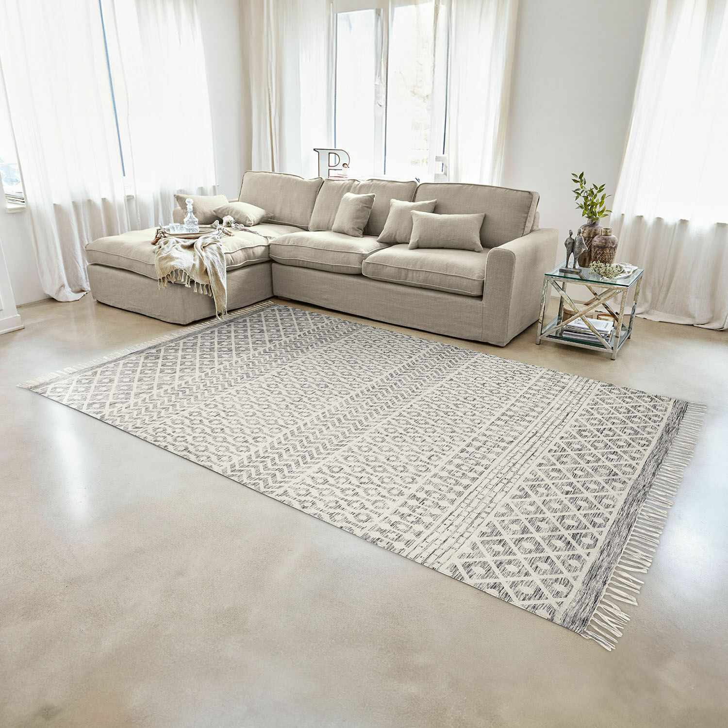Sofá rinconero beige de tela en sala luminosa con alfombra de patrones geométricos y mesa de cristal