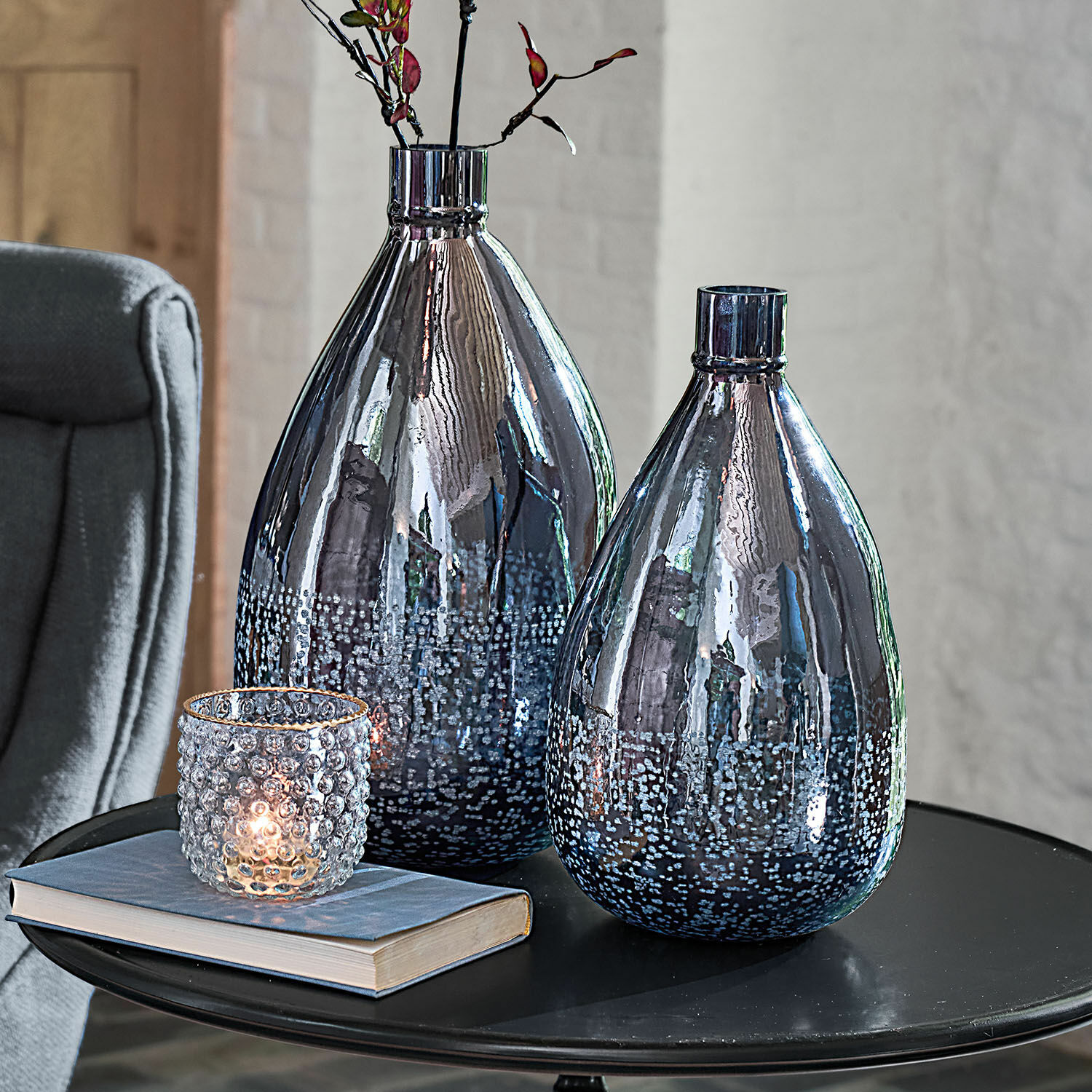 Set de 2 jarrones Qilevon Dos jarrones decorativos de vidrio ahumado con diseño de burbujas sobre mesa negra con libro y portavelas