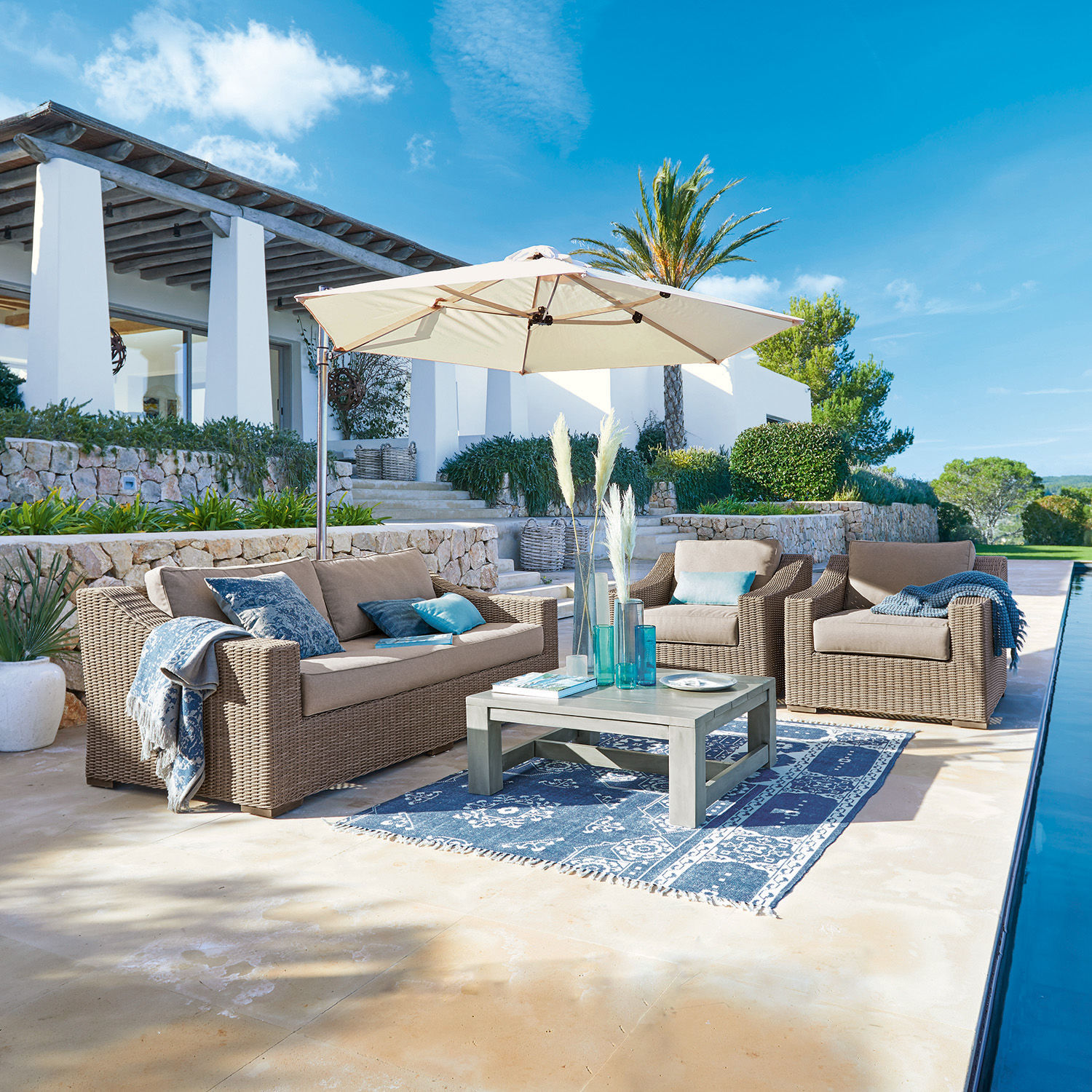 Set de asientos Chestingdale Conjunto de muebles de jardín de ratán beige con sombrilla y alfombra azul en terraza soleada