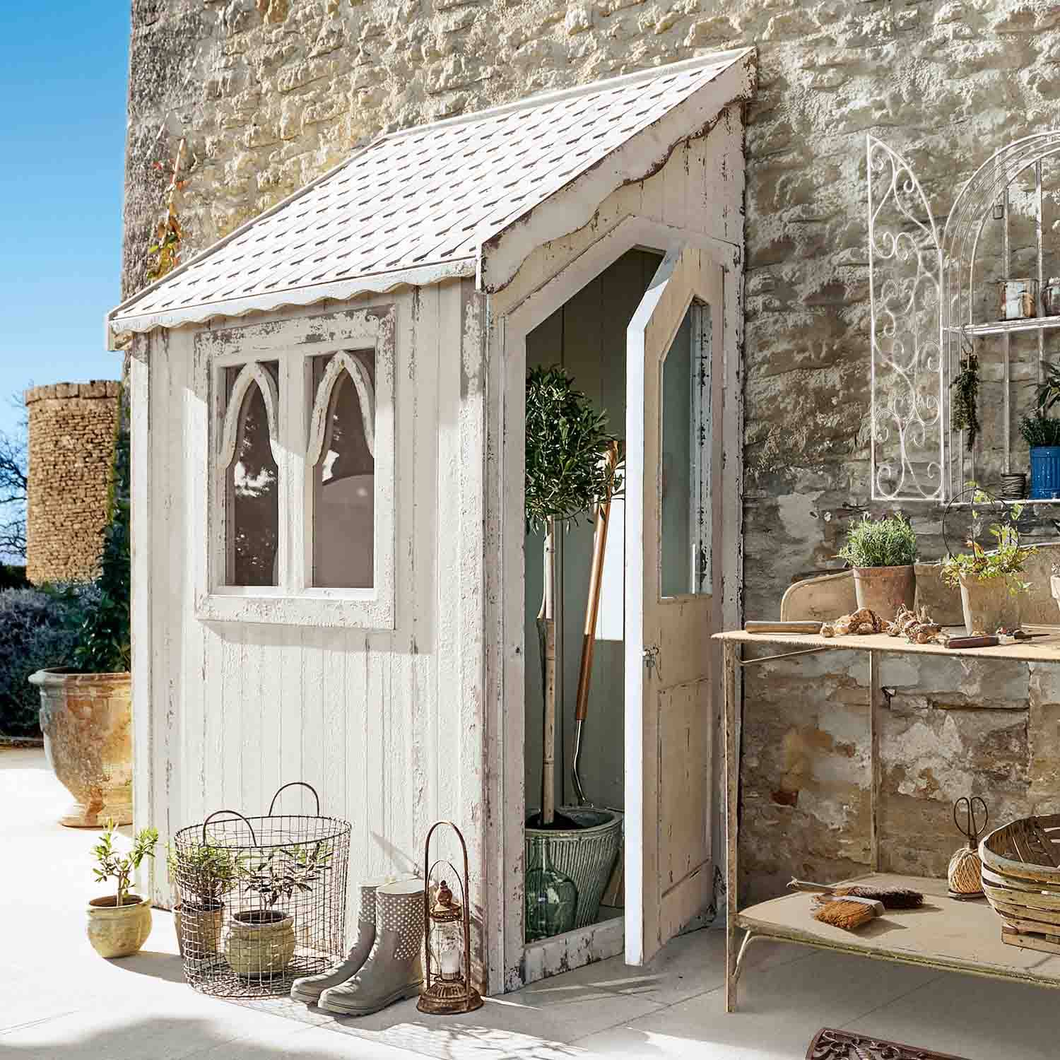 Pequeño cobertizo de jardín de madera blanca con ventanas y puerta abierta, herramientas y decoración