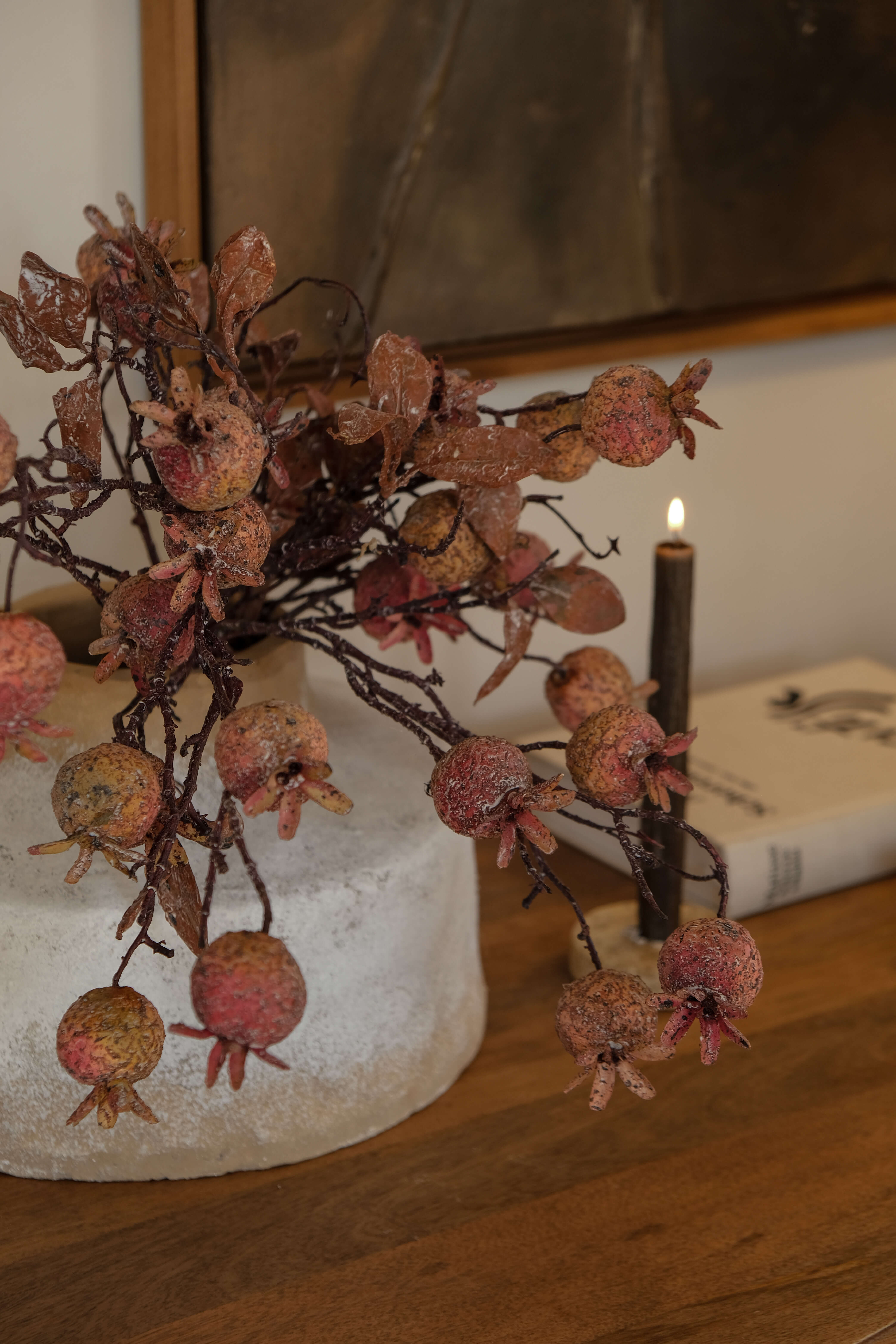 Rama decorativa con frutos de granada en tonos naturales sobre base clara en mesa de madera