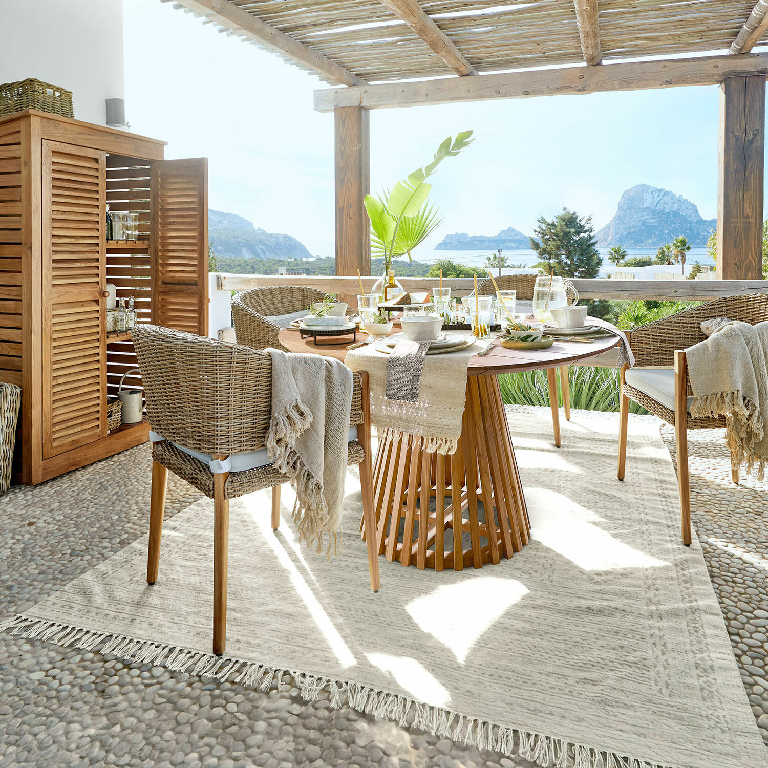 Alfombra para interior y exterior Savagnac Comedor en terraza con mesa de madera y sillas de mimbre beige, vista al mar y decoración natural