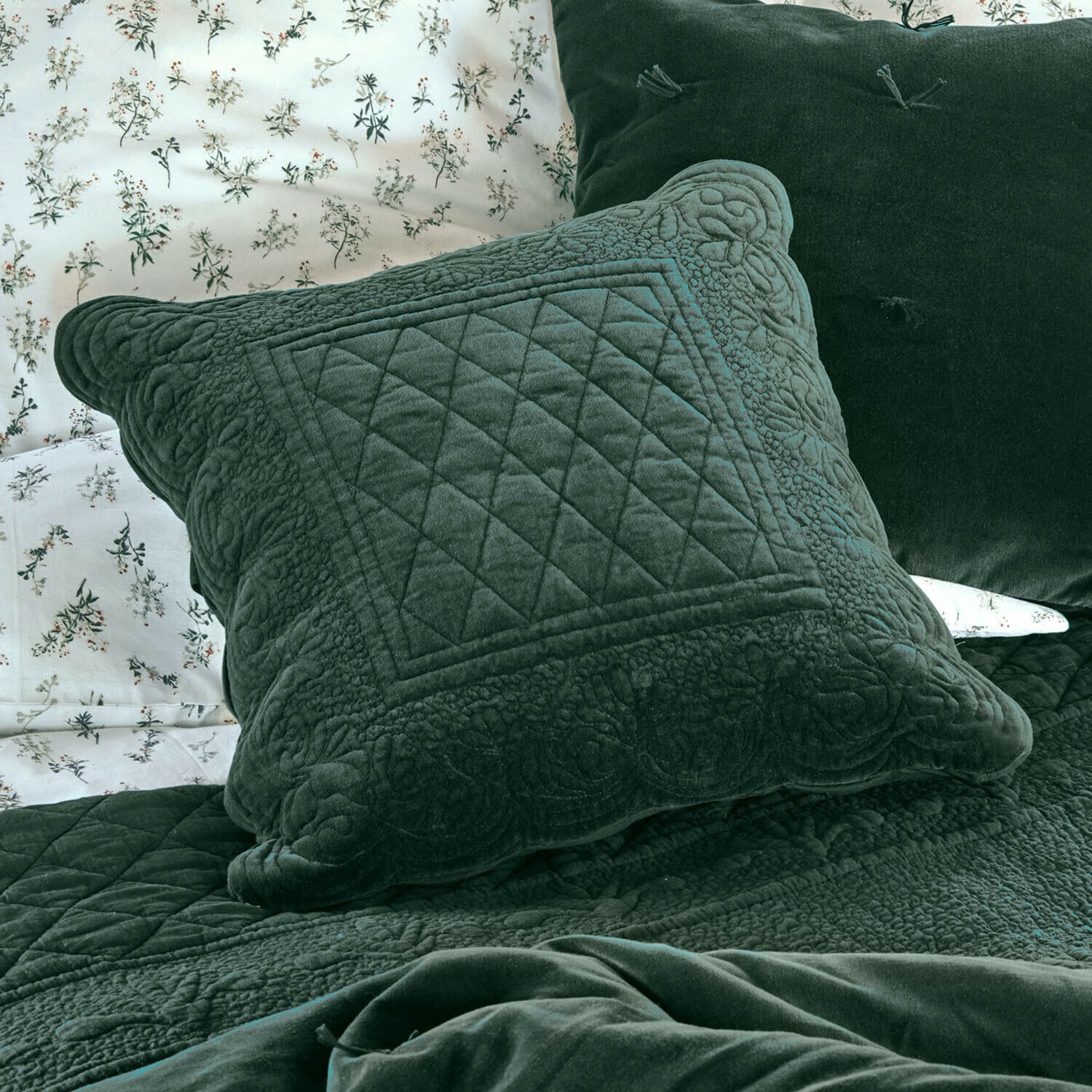 Funda de cojín Lunévois Cojín verde de terciopelo con diseño acolchado sobre cama con ropa de cama floral y manta