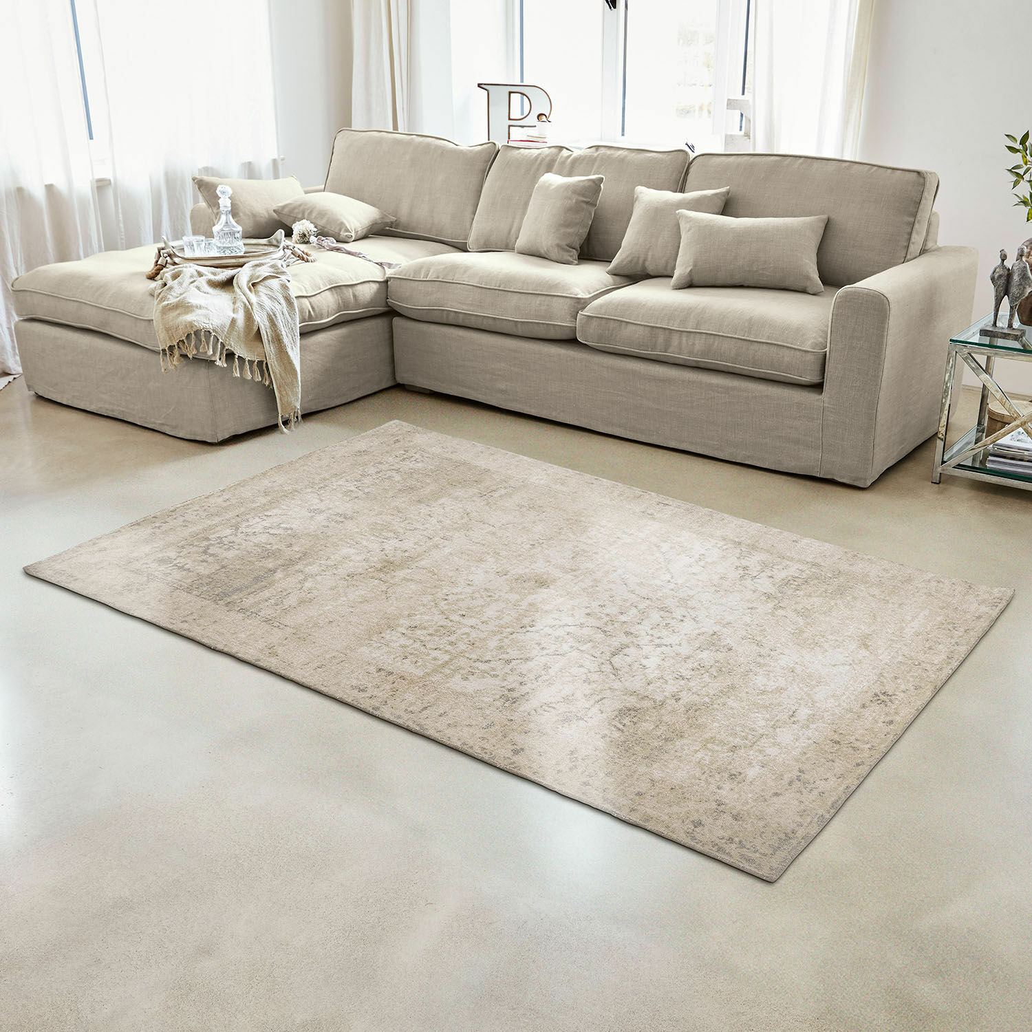 Sofá esquinero beige de tela con cojines y alfombra clara en sala de estar moderna