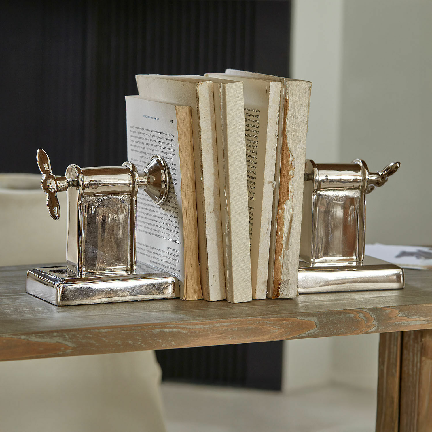 Set de 2 sujetalibros Iskora Sujetalibros metálicos plateados con forma de tornillo sobre mesa de madera, decoración hogar