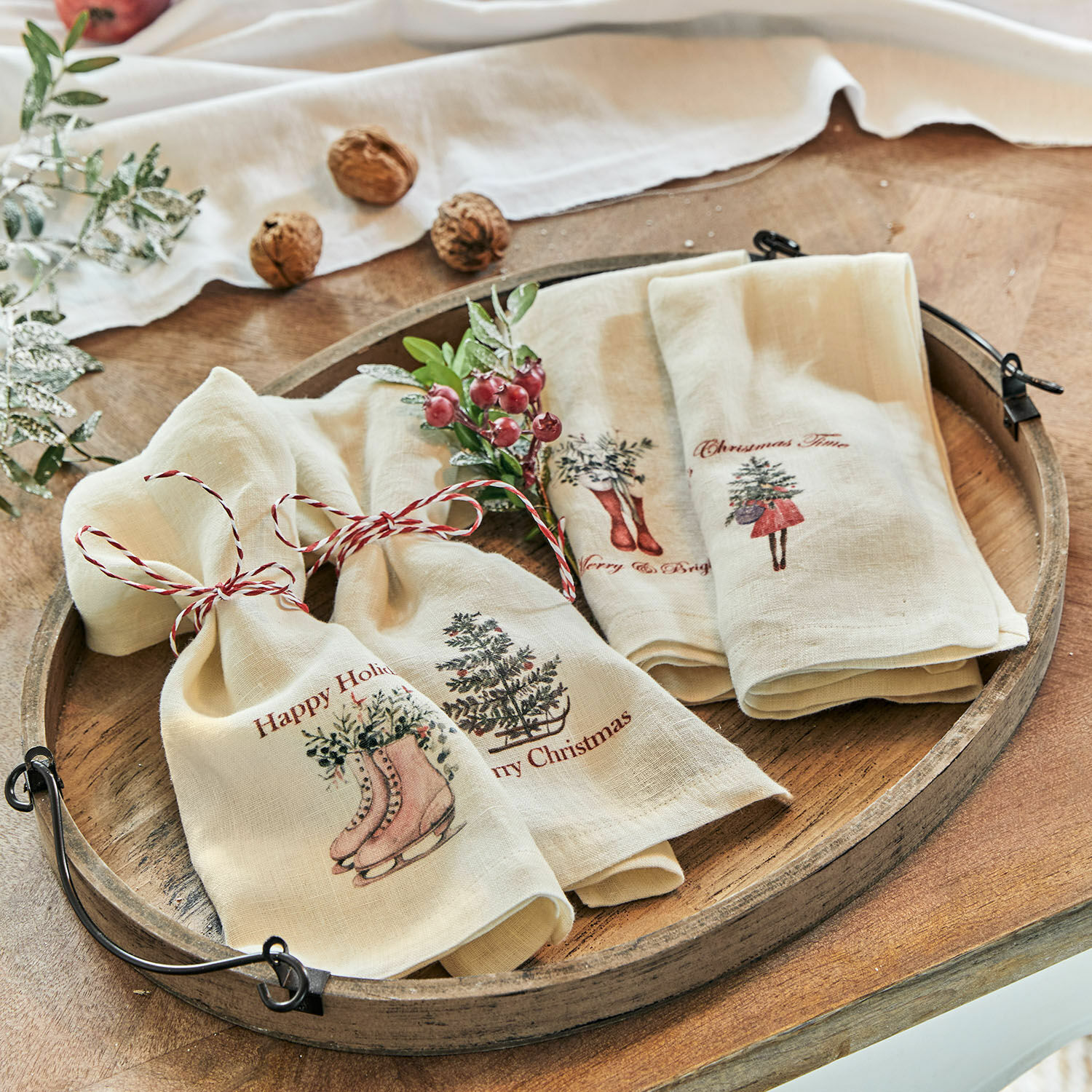 Set de 4 servilletas Merry & Bright Paños de lino crema con motivos navideños y cuerda roja sobre bandeja de madera rústica