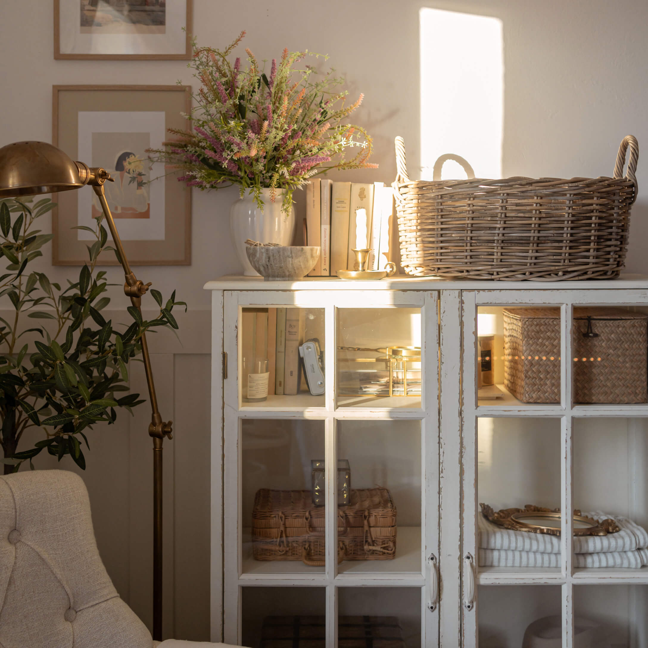 Aparador blanco de madera con puertas de cristal, cesta de mimbre y decoración en salón luminoso