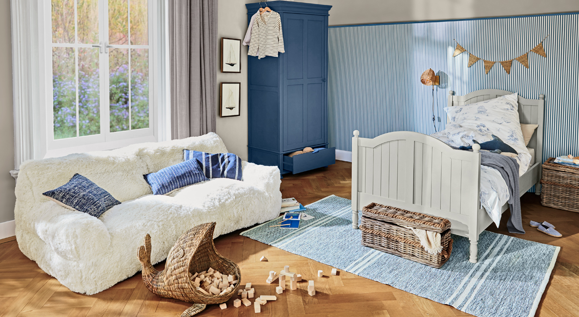 Acogedora habitación infantil con cama de madera blanca, armario azul y sofá blanco suave con cojines azules