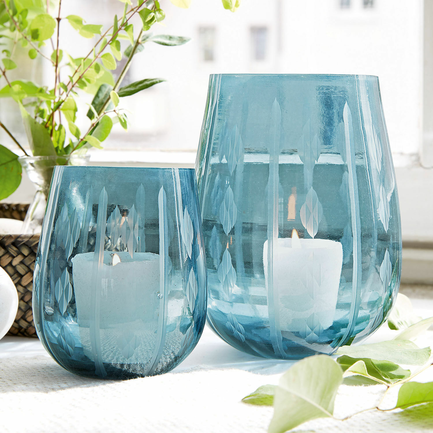 Dos portavelas de vidrio azul con diseño grabado de hojas, decoración interior con velas blancas