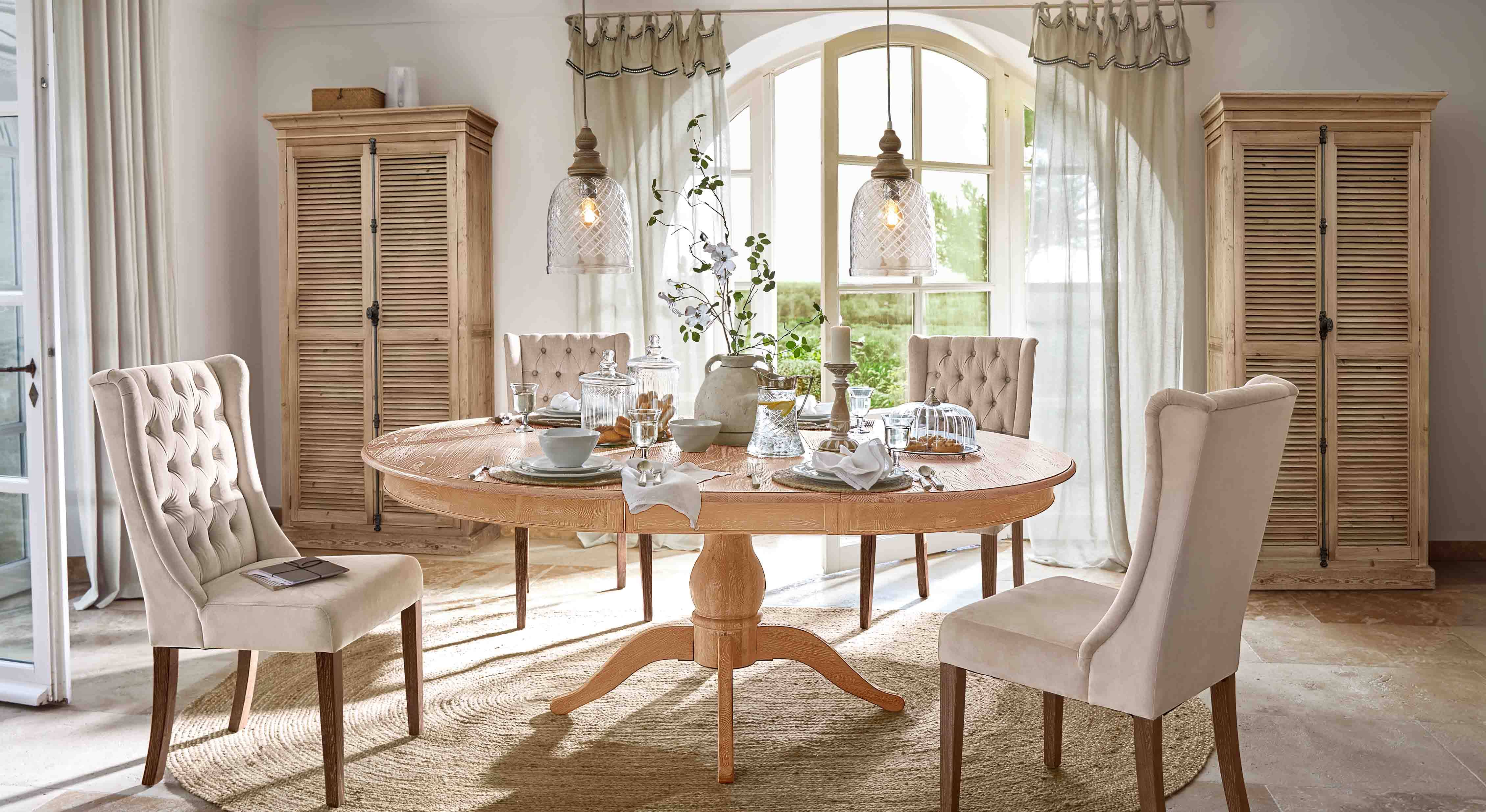 Comedor con mesa redonda de madera clara y sillas tapizadas beige en estilo clásico