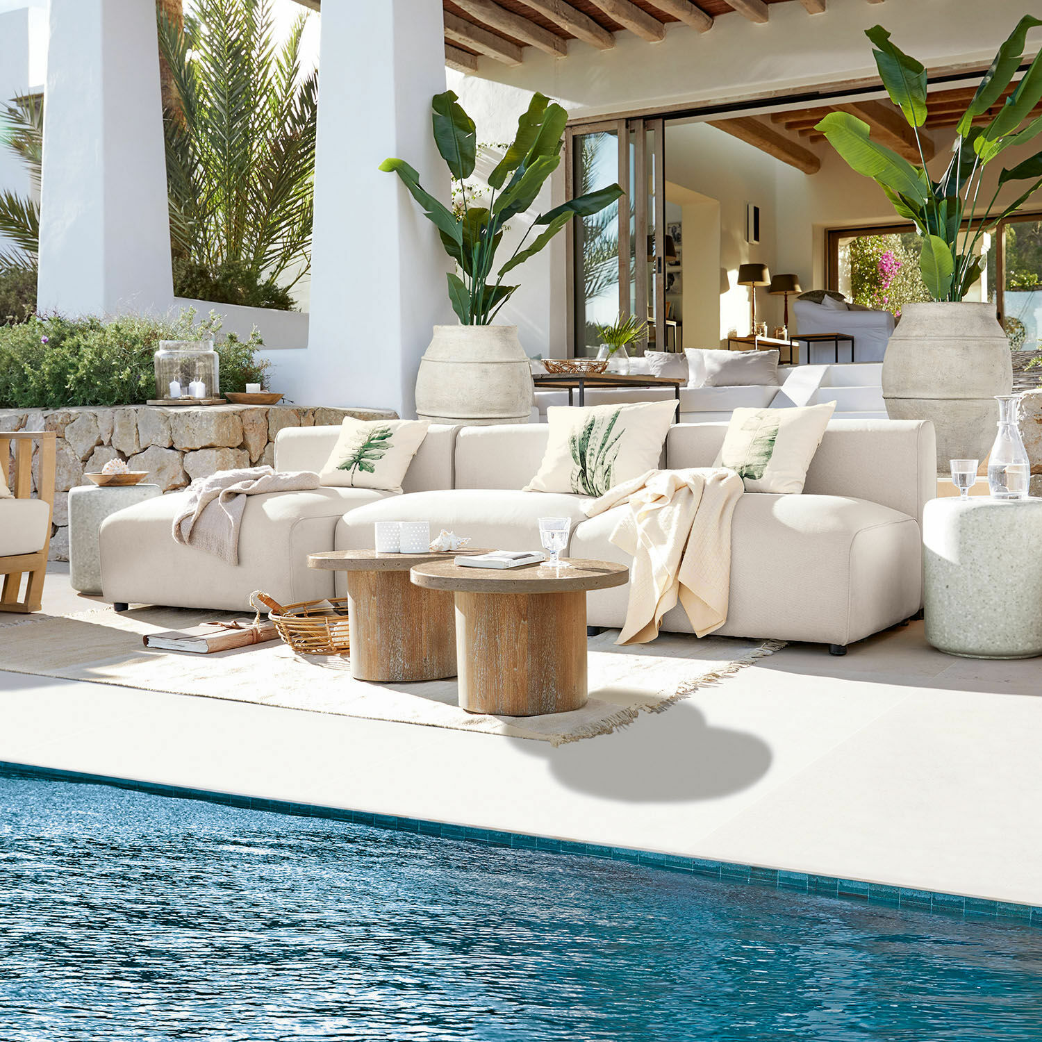Grupo de asientos Vézère Sofá beige de tela en terraza junto a piscina con mesas de madera y cojines decorativos