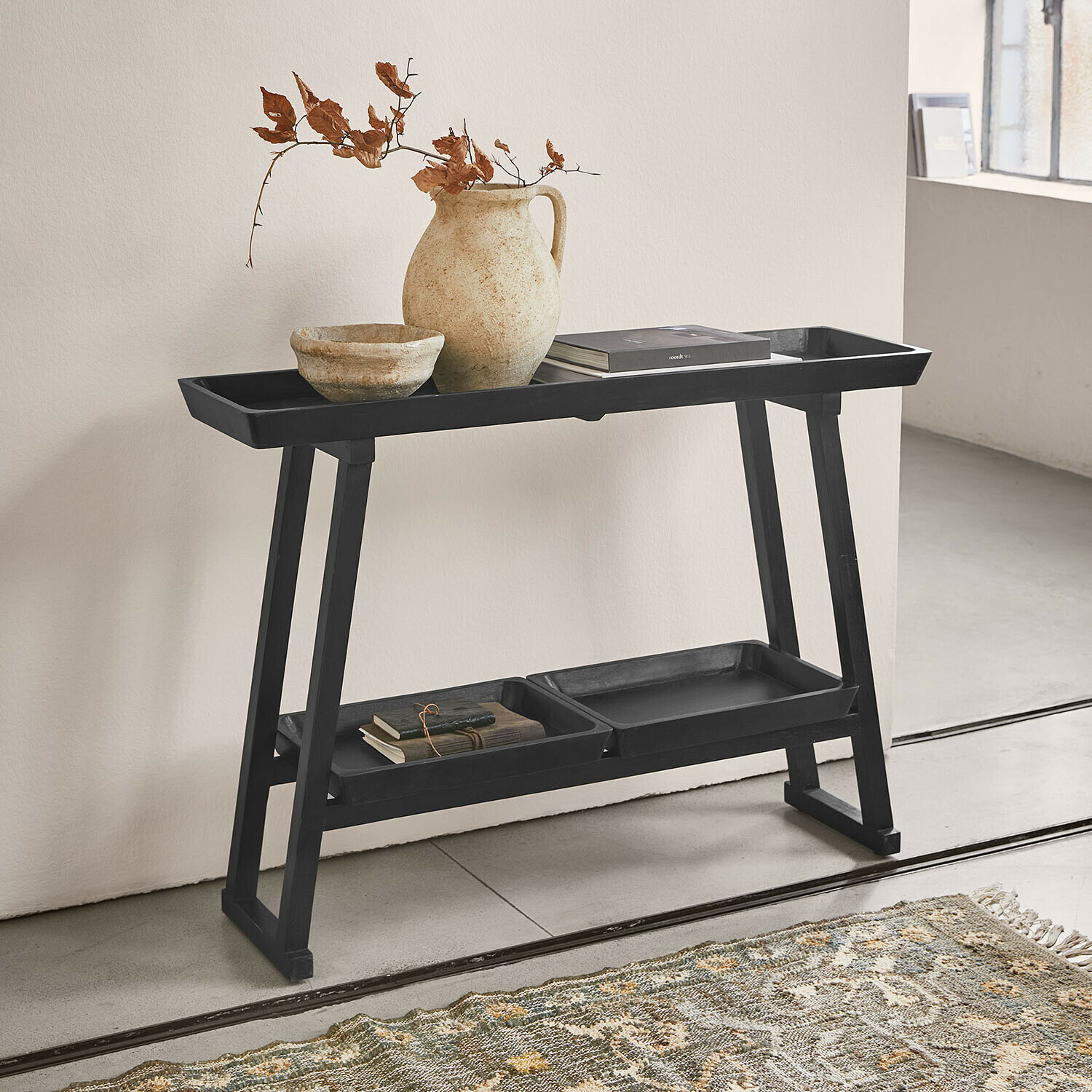 Consola Ivywood Mesa auxiliar negra de madera con estantes, jarrón de cerámica y libros en interior minimalista