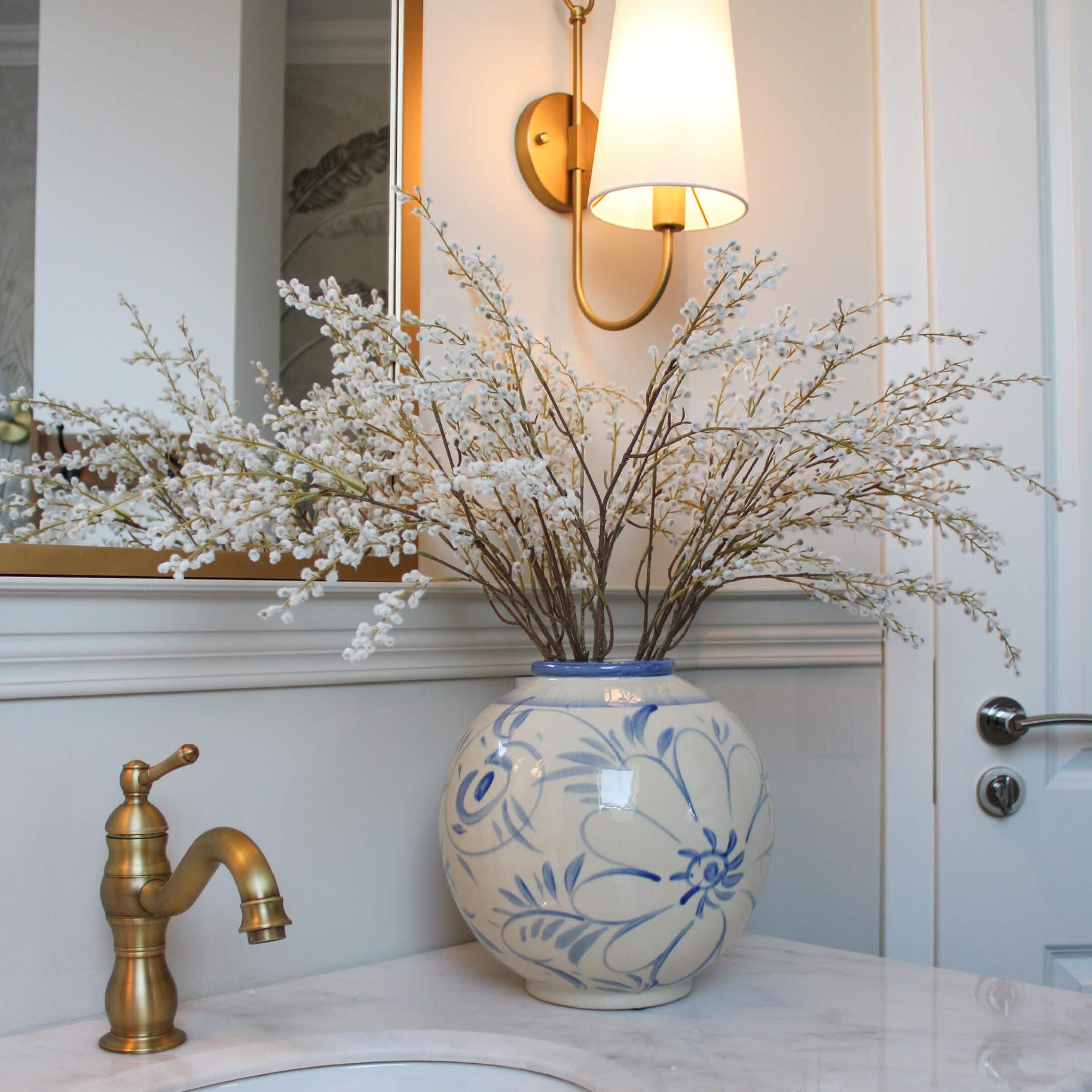 Jarrón de cerámica con diseño floral azul y ramas de flores blancas sobre encimera de mármol en baño