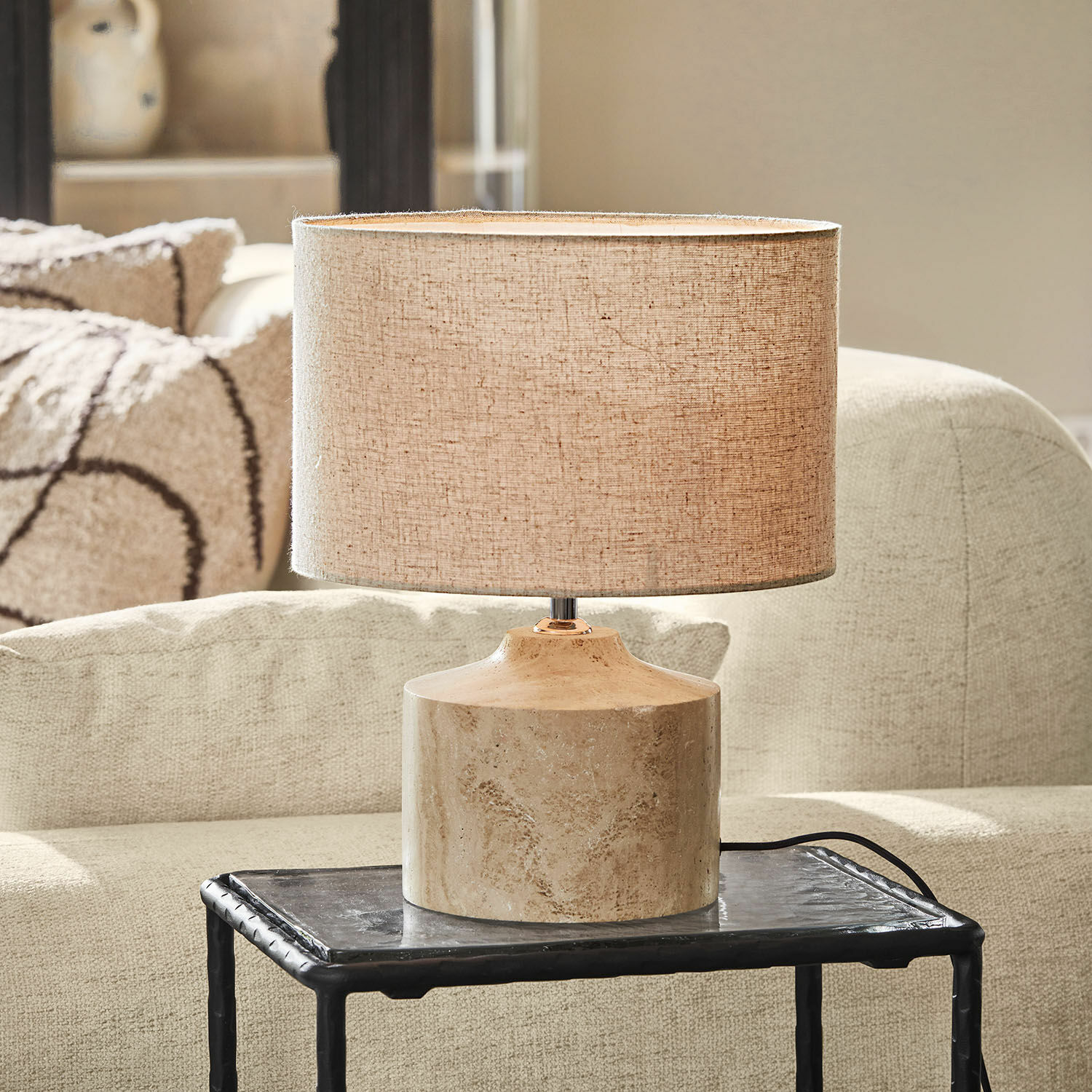 Lámpara de mesa con pantalla beige y base de mármol sobre mesa negra en sala de estar