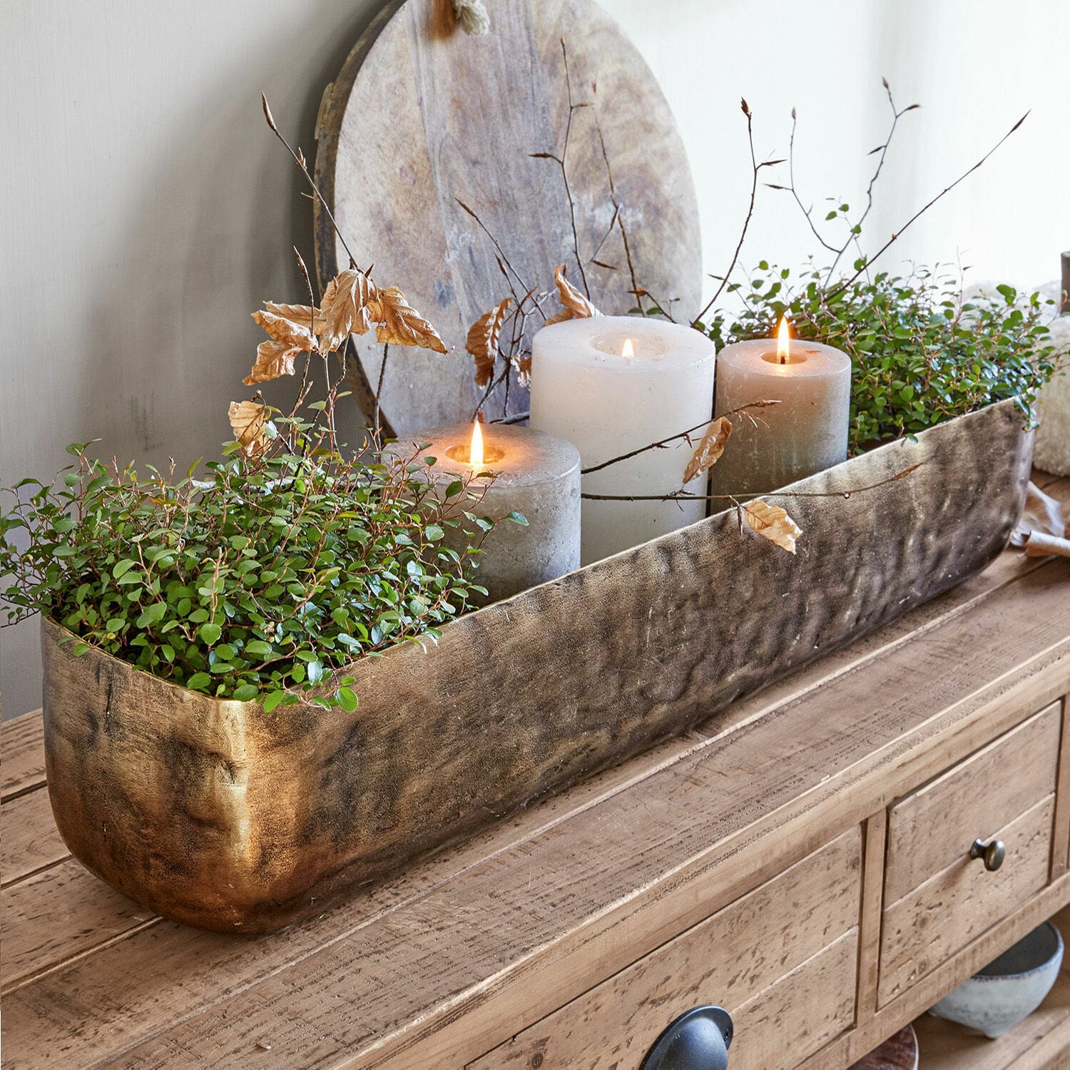 Recipiente Skye Maceta decorativa de metal dorado con plantas verdes y tres velas sobre mesa de madera