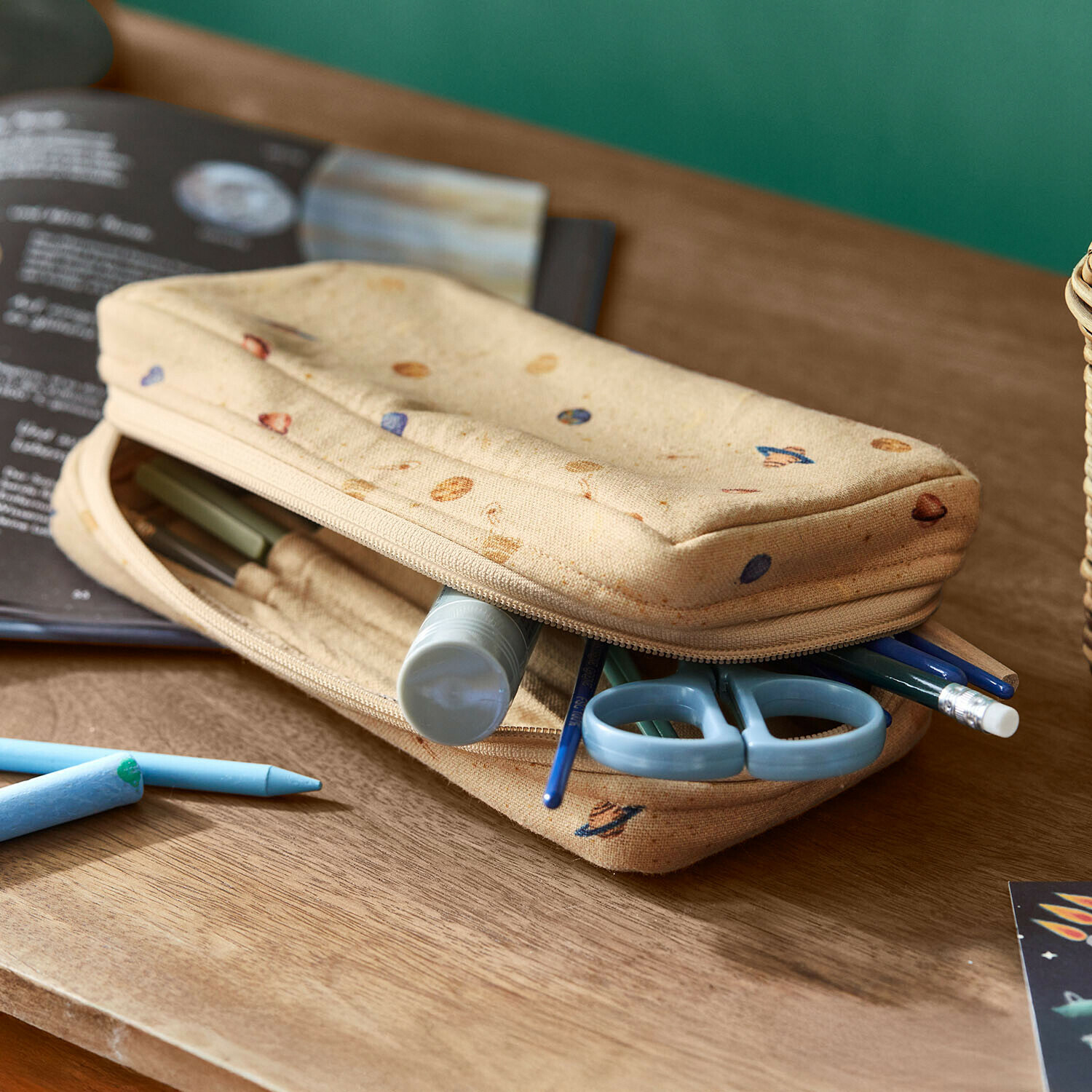 Estuche Xeltra Estuche beige de tela con diseño de planetas, tijeras azules y material de escritura sobre mesa de madera