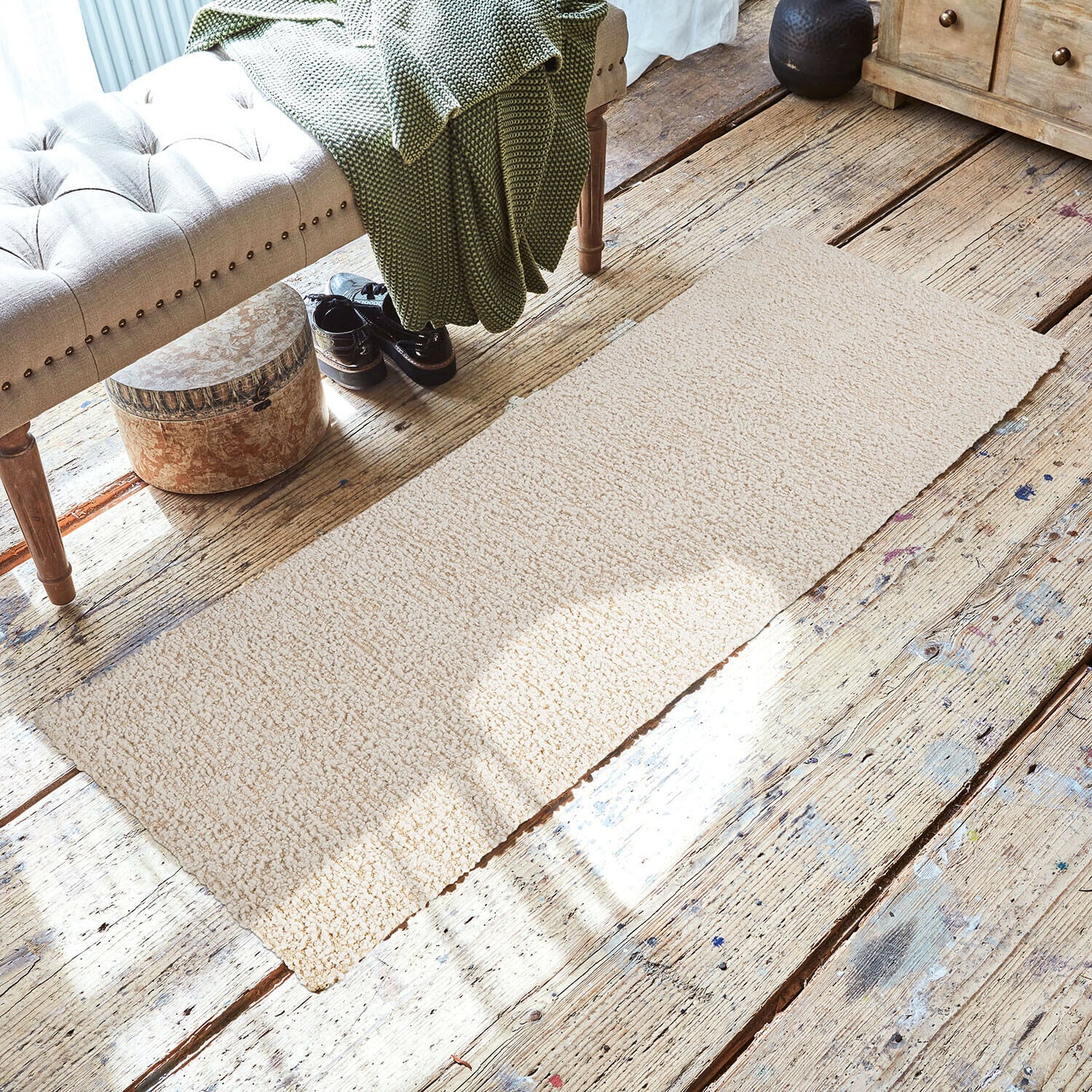 Alfombra Kaleema Alfombra beige de material suave sobre suelo de madera en interior acogedor con banco y manta verde