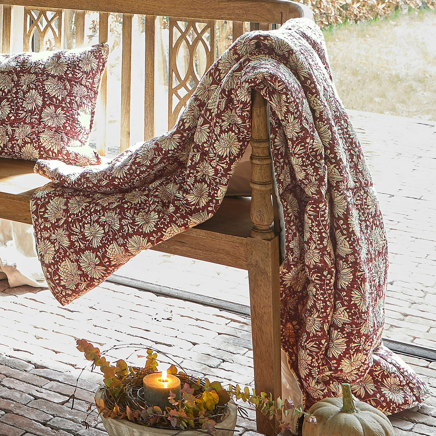Plaid Soleique Manta y cojín rojos con diseño floral sobre banco de madera, decoración otoñal con calabaza y vela