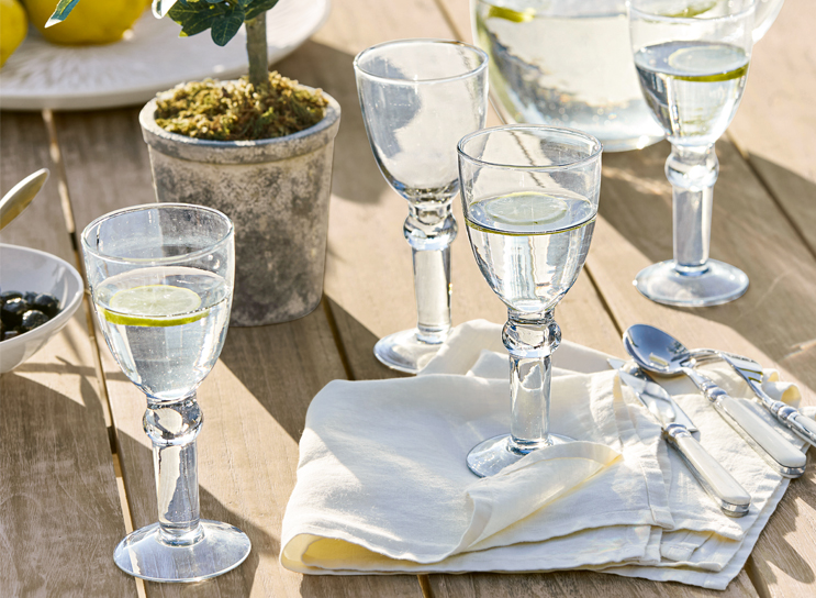 Vasos de agua con limón sobre mesa de madera con servilleta blanca y cubiertos, estilo mediterráneo