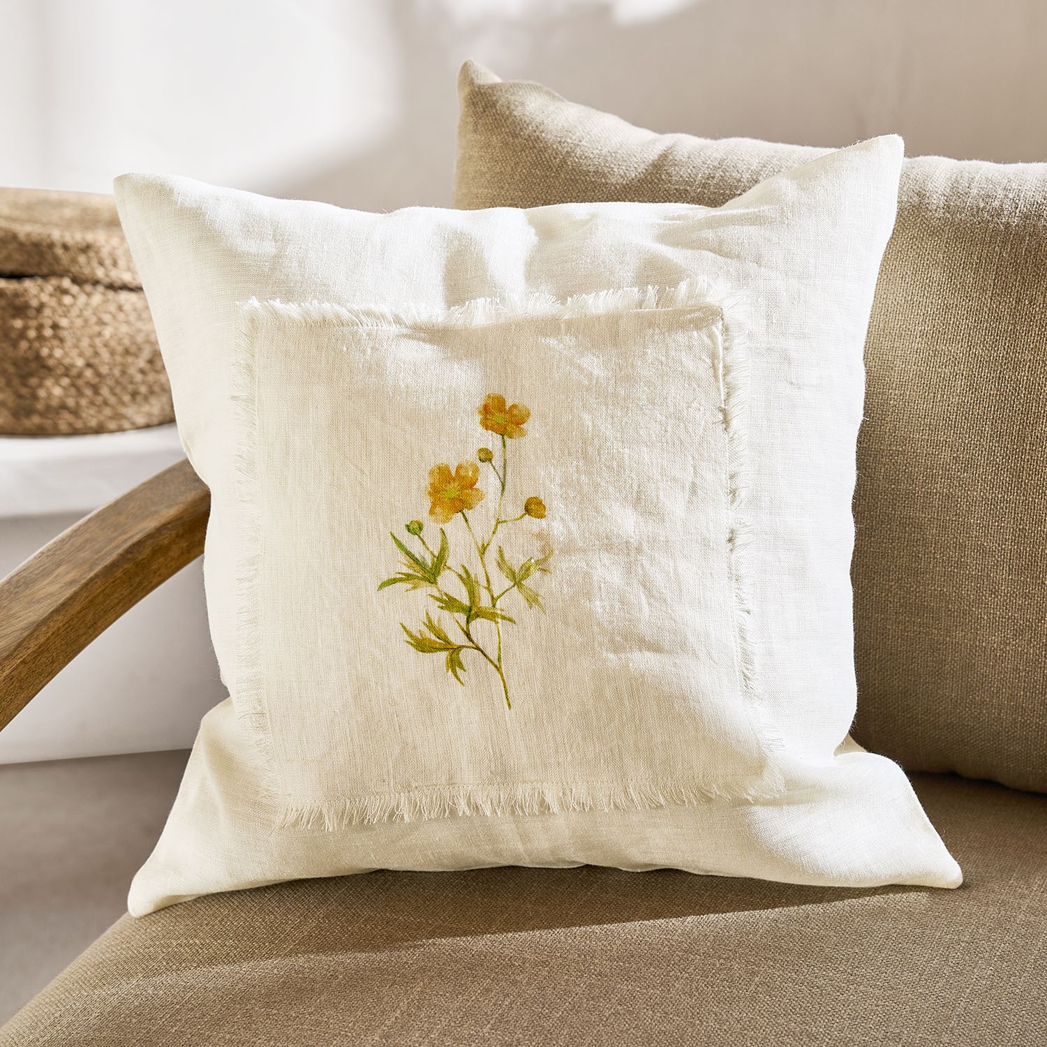 Cojín decorativo de lino color crema con estampado floral amarillo y bordes deshilachados