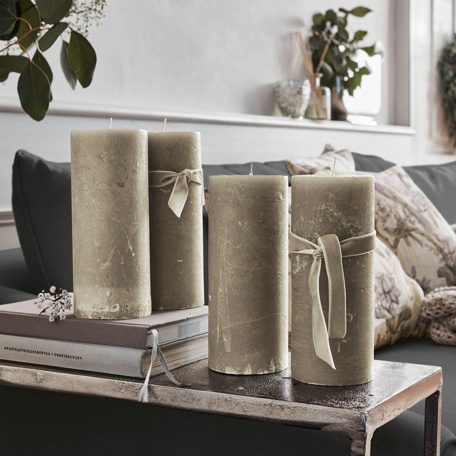 Conjunto de cuatro velas decorativas beige con lazos sobre mesa metálica en sala de estar