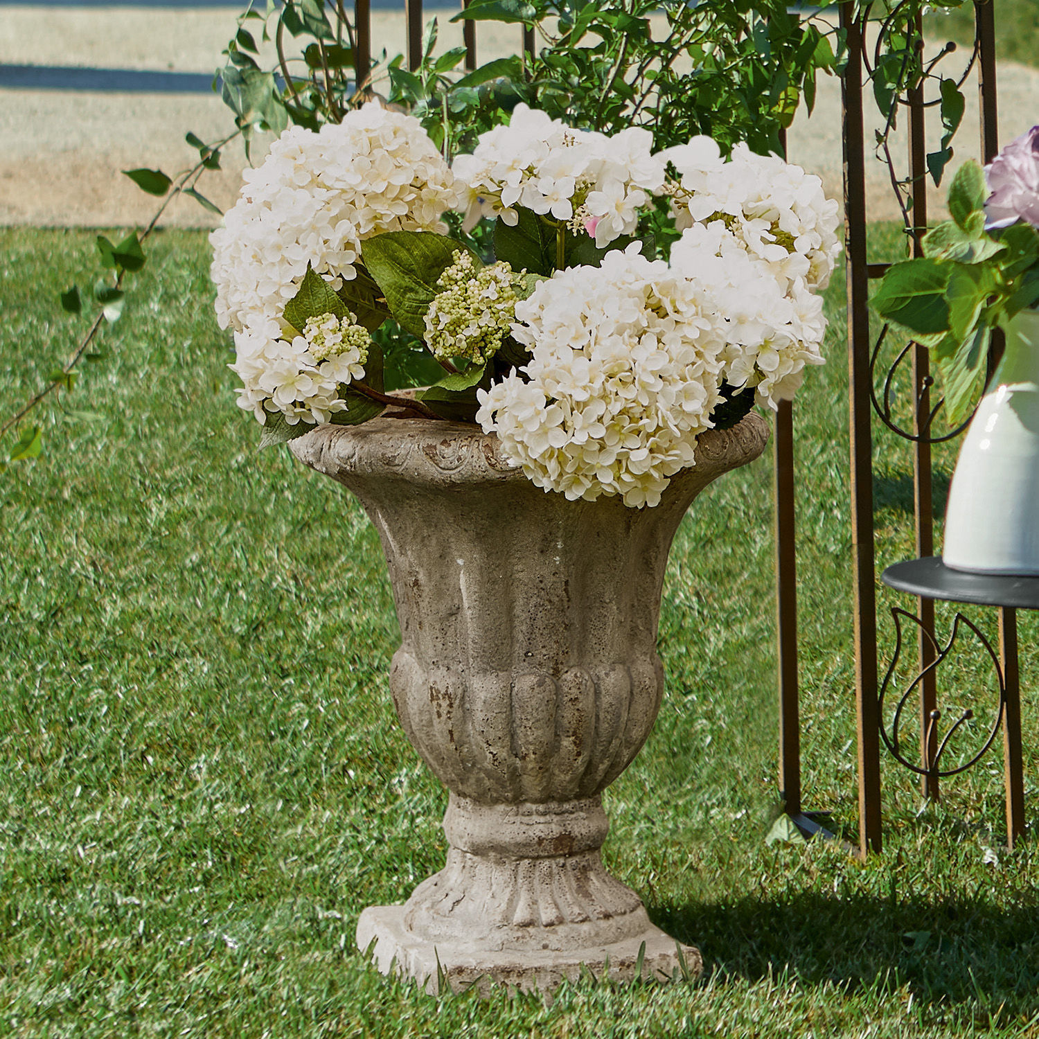 Maceta decorativa de hormigón estilo clásico con hortensias blancas sobre césped verde