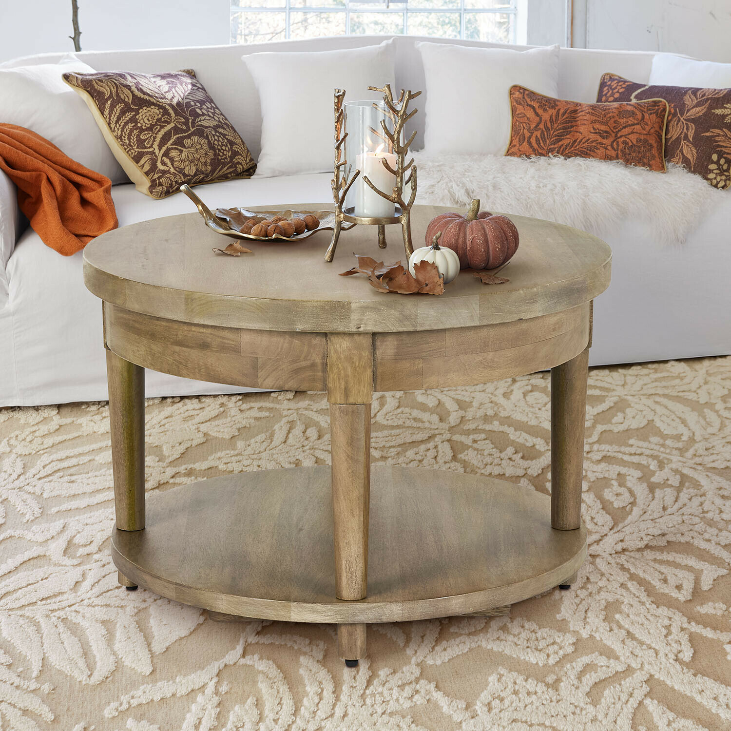 Mesa de centro Talinar Mesa de centro redonda de madera color natural con decoración de vela y calabazas sobre alfombra beige