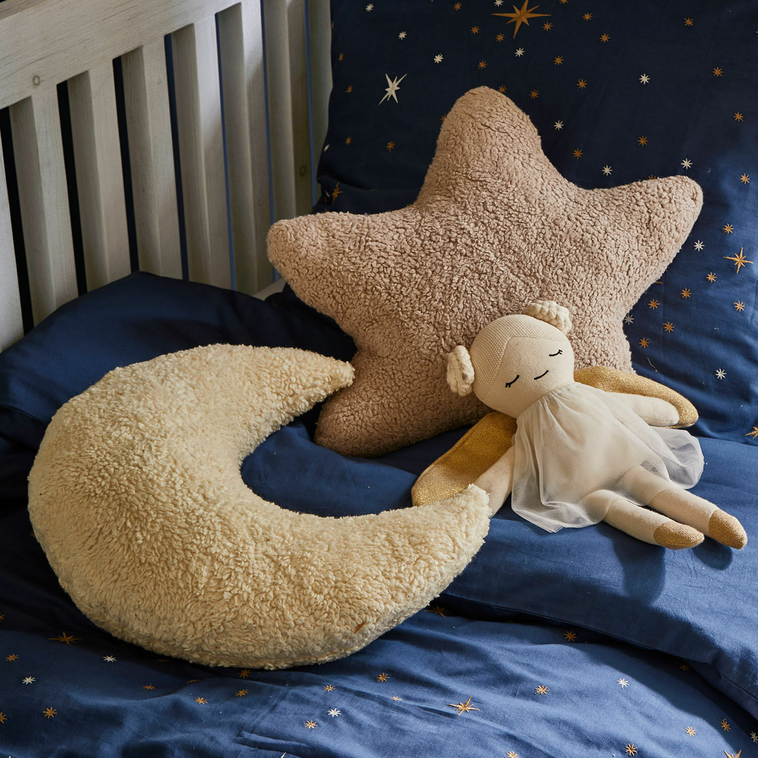 Set de 2 cojines Jollymoon Cojines suaves en forma de estrella y luna de material peludo beige sobre ropa de cama azul con estrellas