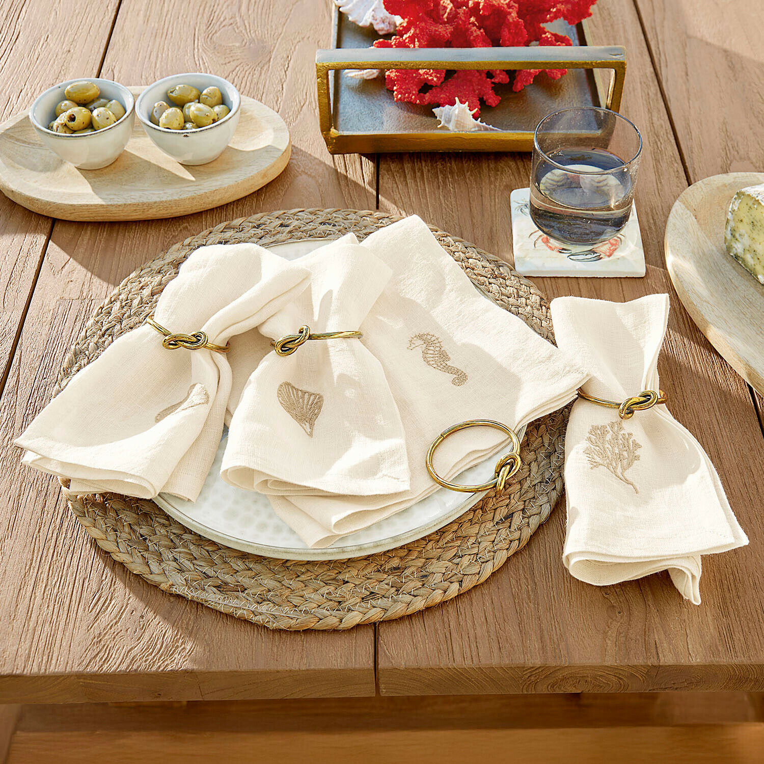 Set de 4 servilletas Celorin Servilletas de lino crema con motivos marinos y anillos dorados sobre mesa de madera para decoración
