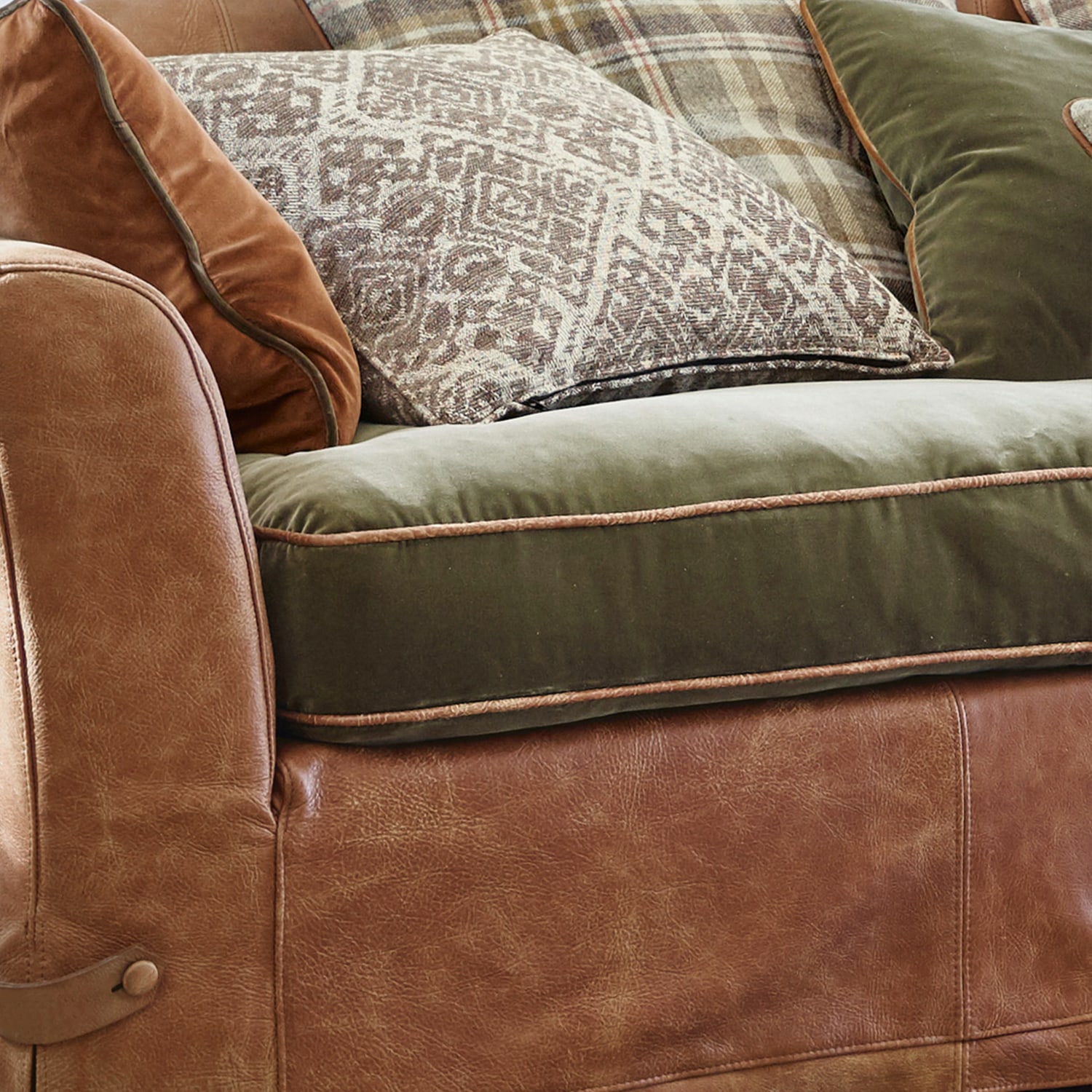Sofá de cuero marrón con asiento de terciopelo verde y cojines decorativos de estilo rústico