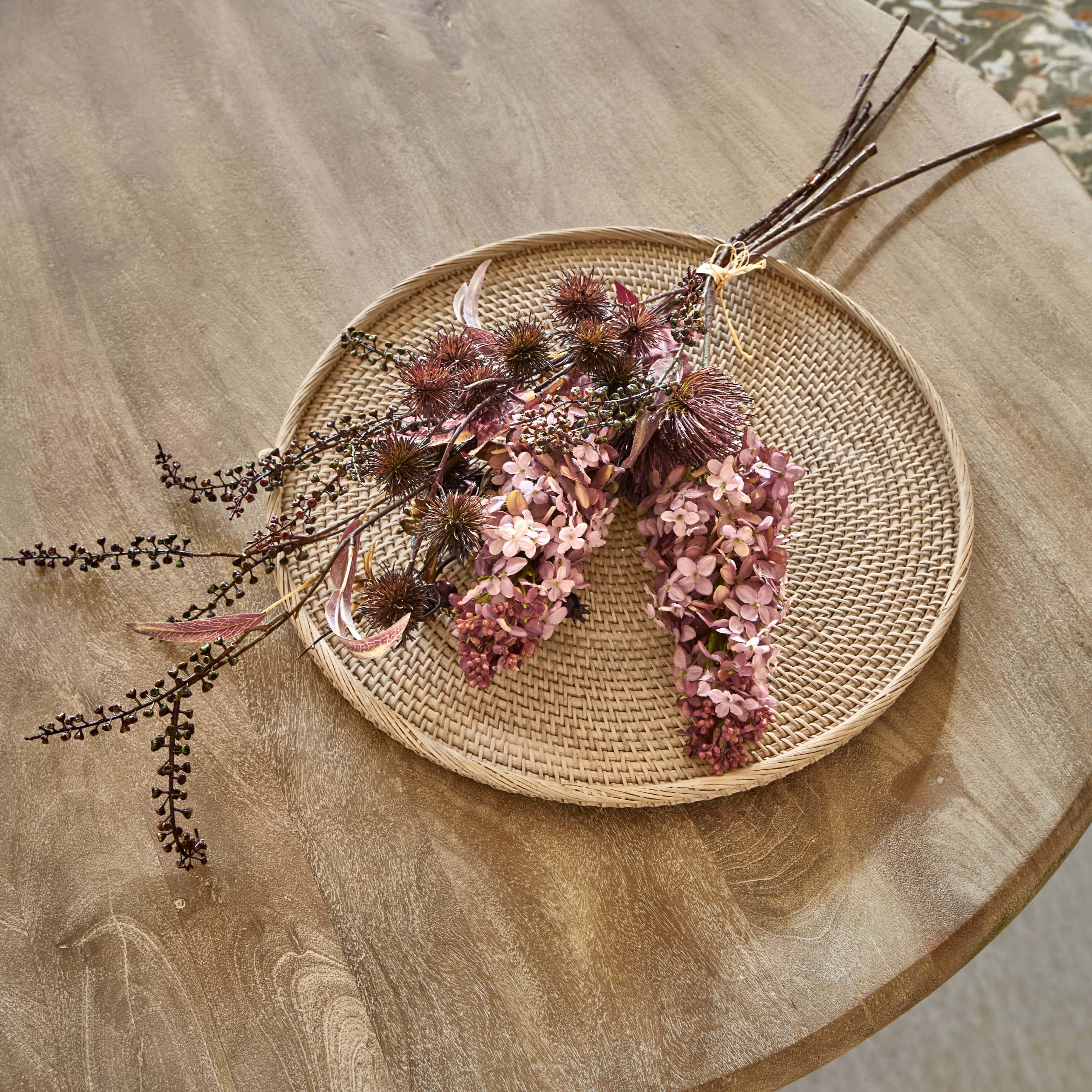 Ramo decorativo de flores secas en tonos rosas y marrones sobre bandeja de ratán trenzado para decoración