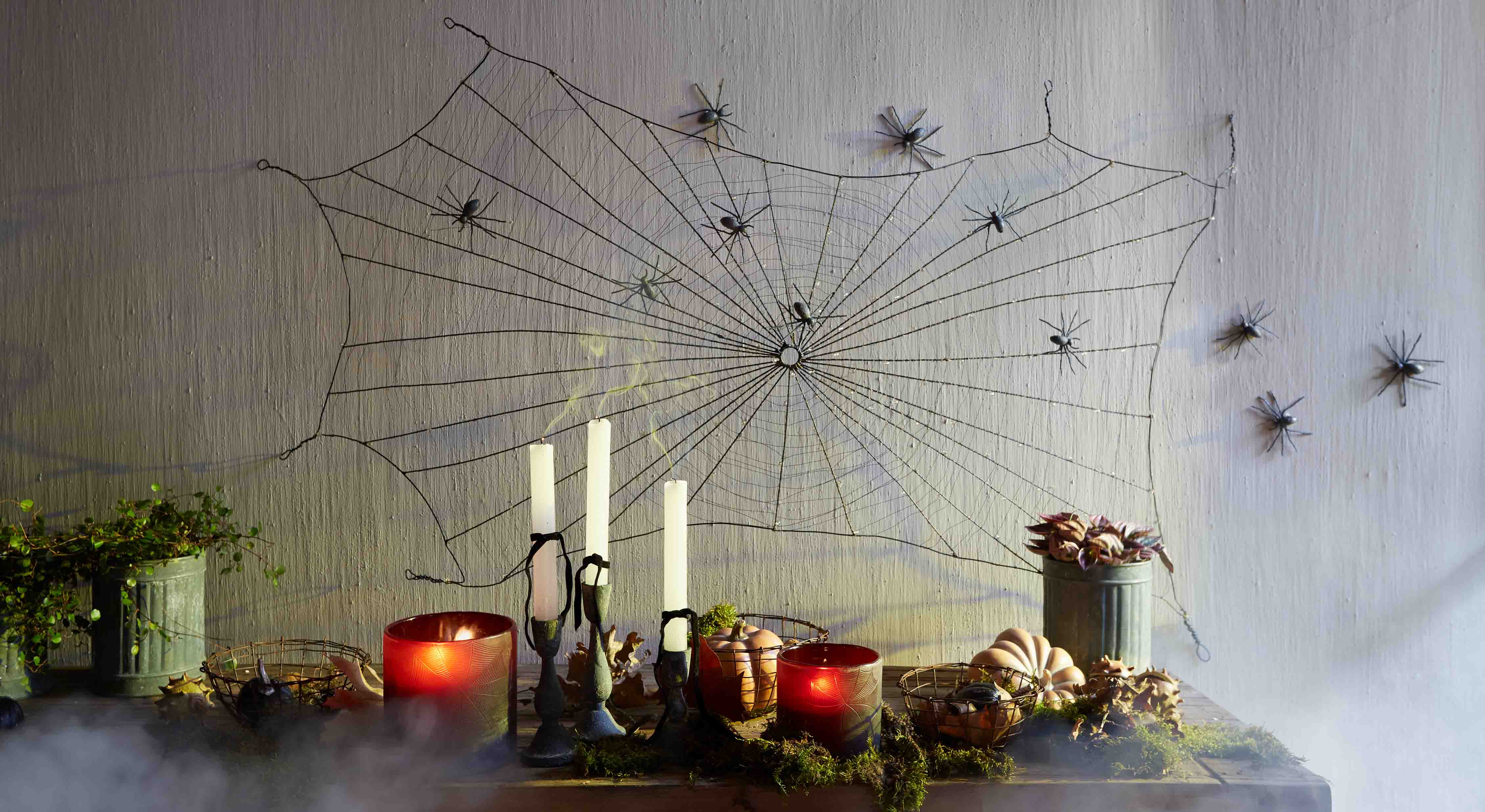 Decoración de Halloween con telaraña negra y arañas de plástico en la pared, velas y calabazas sobre la mesa