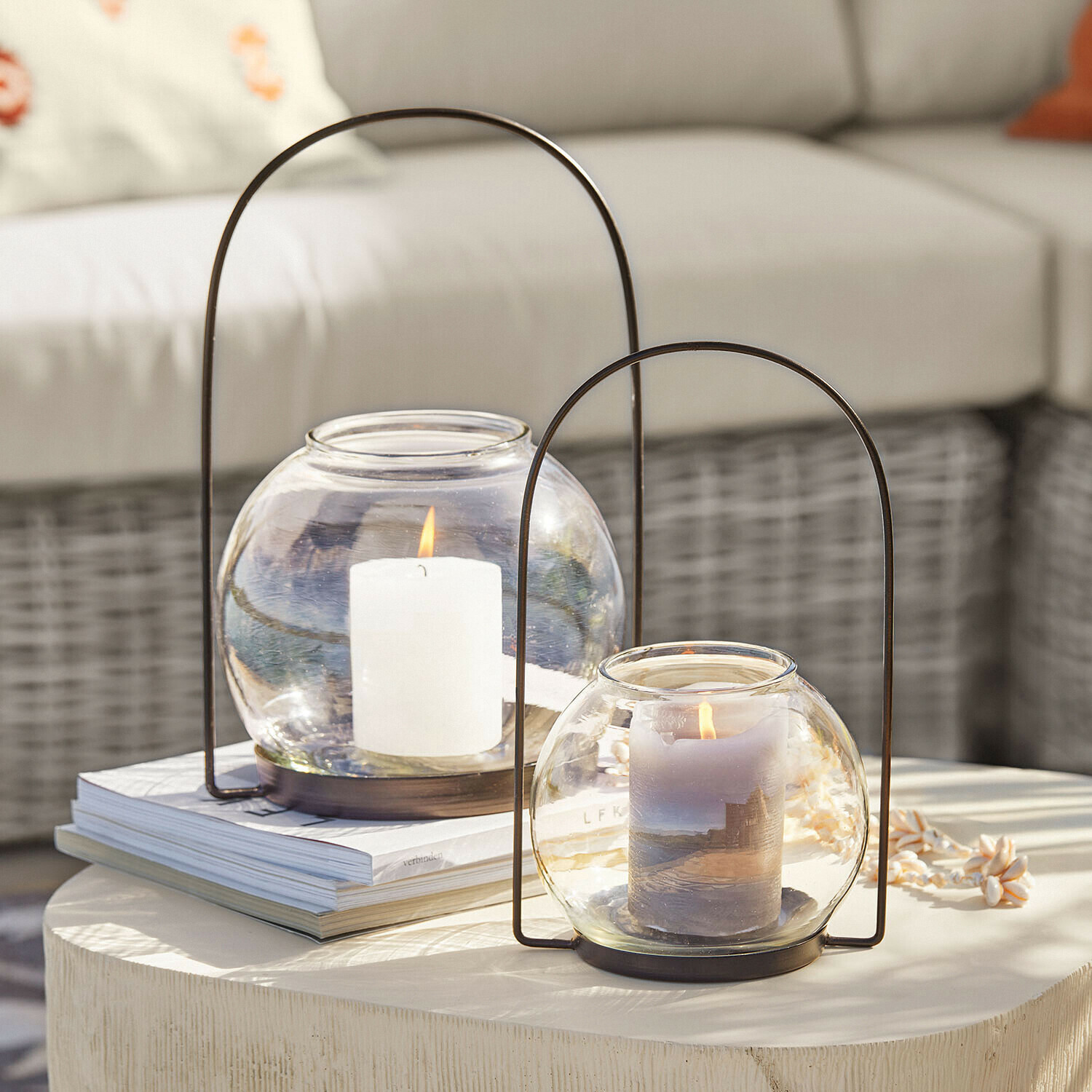 Set de 2 portavelas Serenaro Dos faroles de vidrio con asas metálicas y velas encendidas sobre una mesa decorativa clara