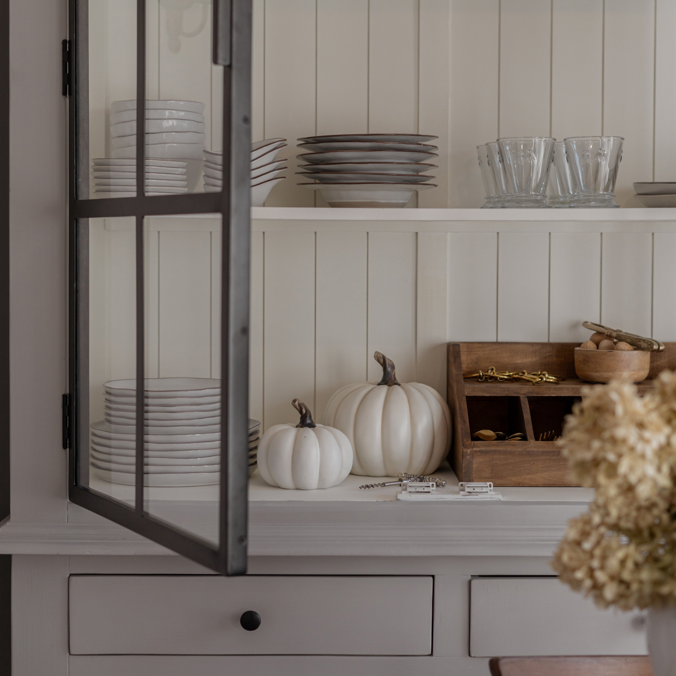 Platos blancos de cerámica y vasos en estante con calabazas blancas decorativas y organizador de madera