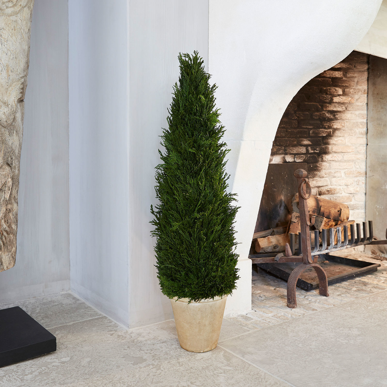 Planta decorativa Arras Planta alta verde en maceta de piedra frente a chimenea blanca y pared de ladrillo