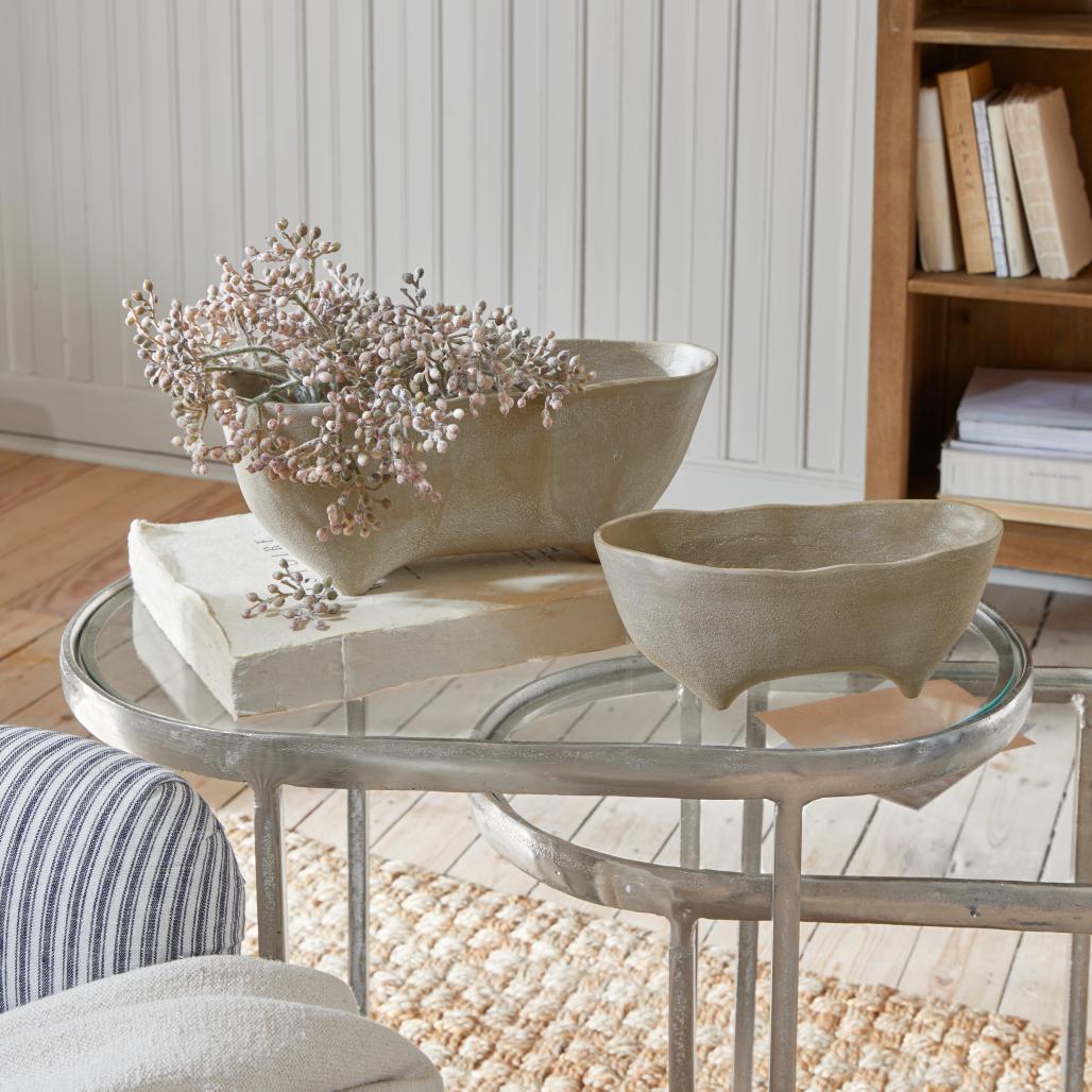 Dos cuencos de cerámica beige con patas sobre mesa de cristal en interior luminoso y acogedor
